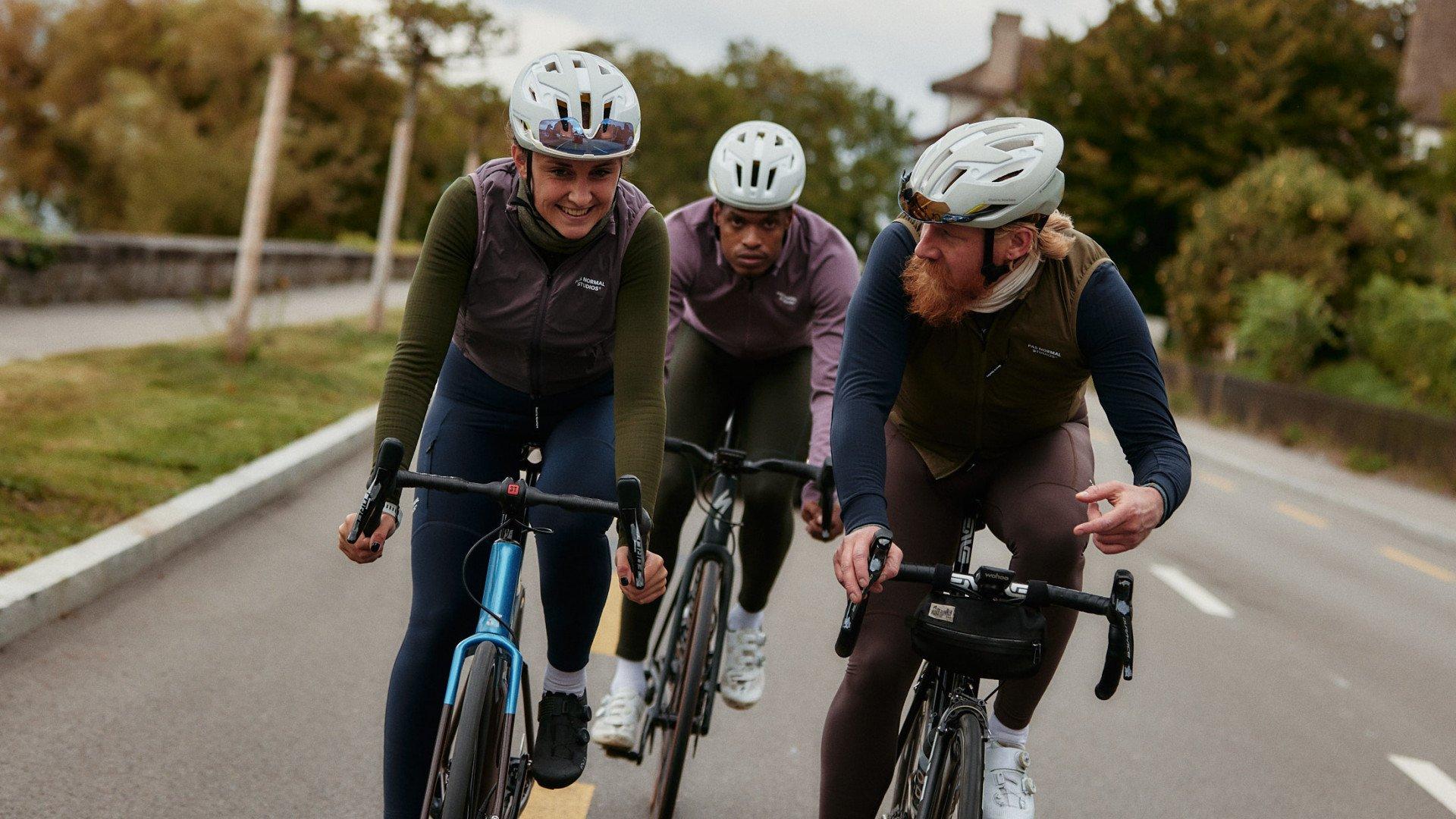 Three cyclists in aerodynamic position on time trial bikes wearing colorful cycling apparel on rural road