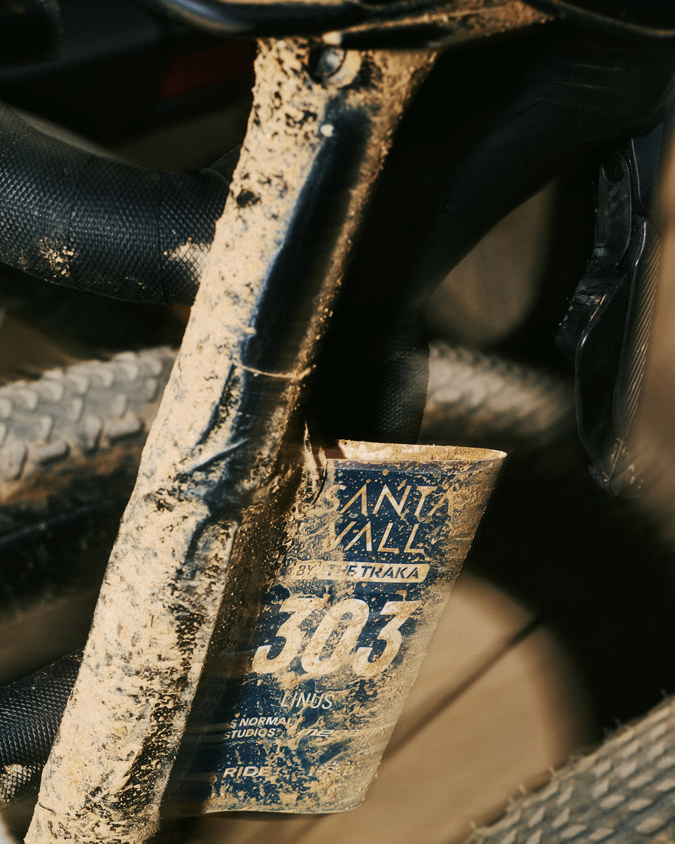 Muddy cycling bike frame with race number 303 attached, covered in dirt from competition