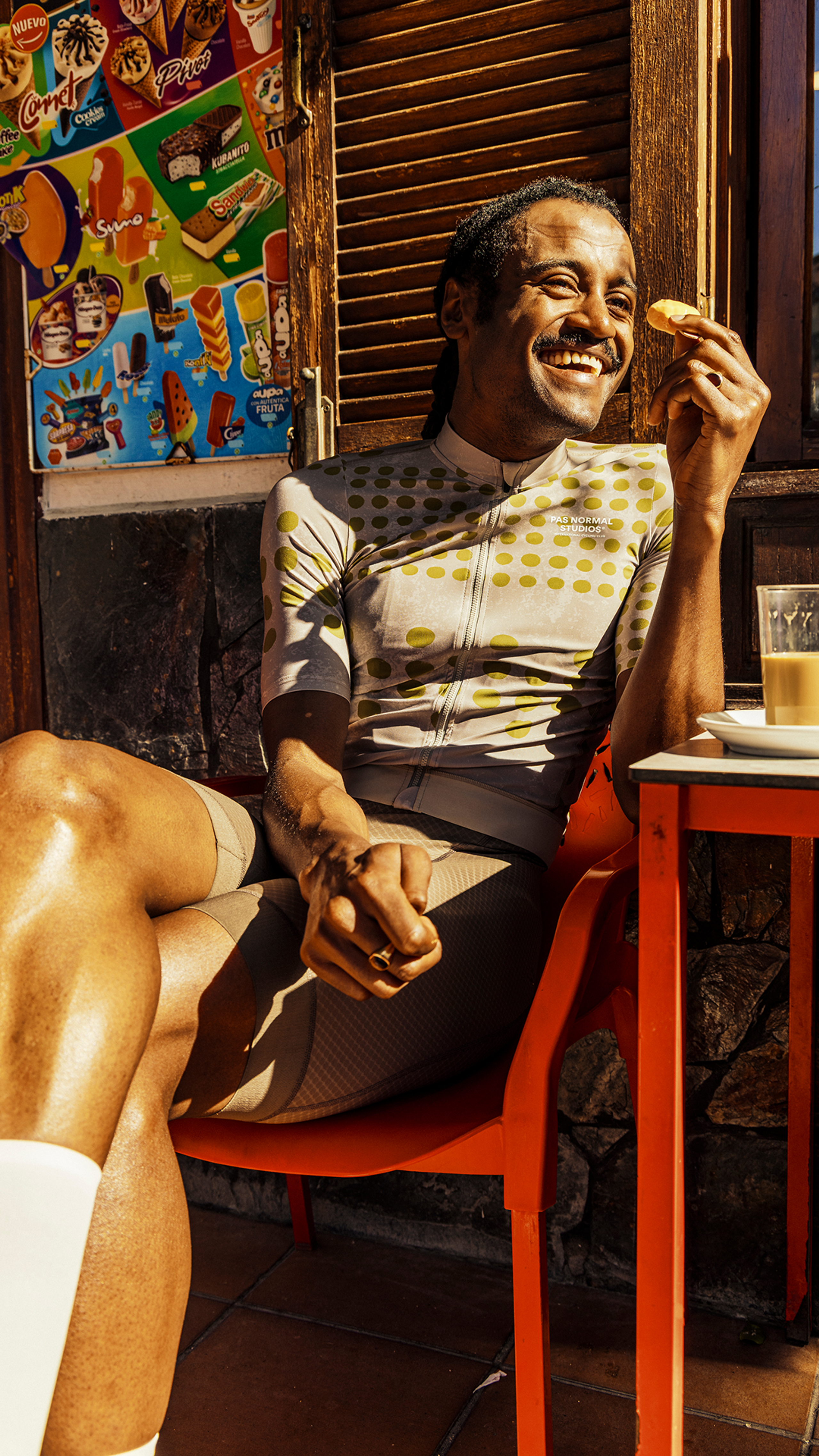 Model wearing white cycling jersey with yellow polka dot pattern at cafe with pastry