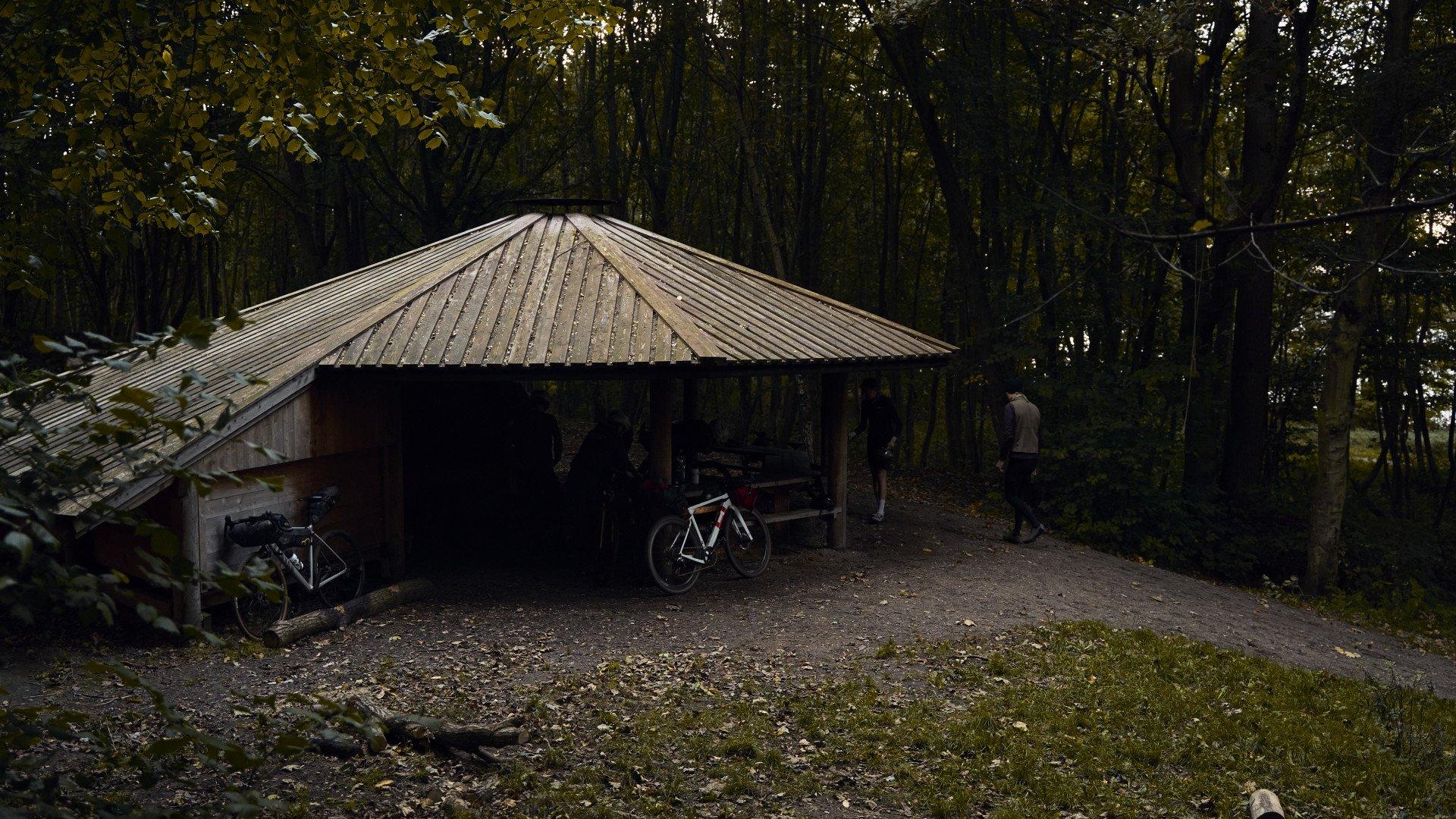 Cyclist at wooden shelter in forest with bikes during autumn ride