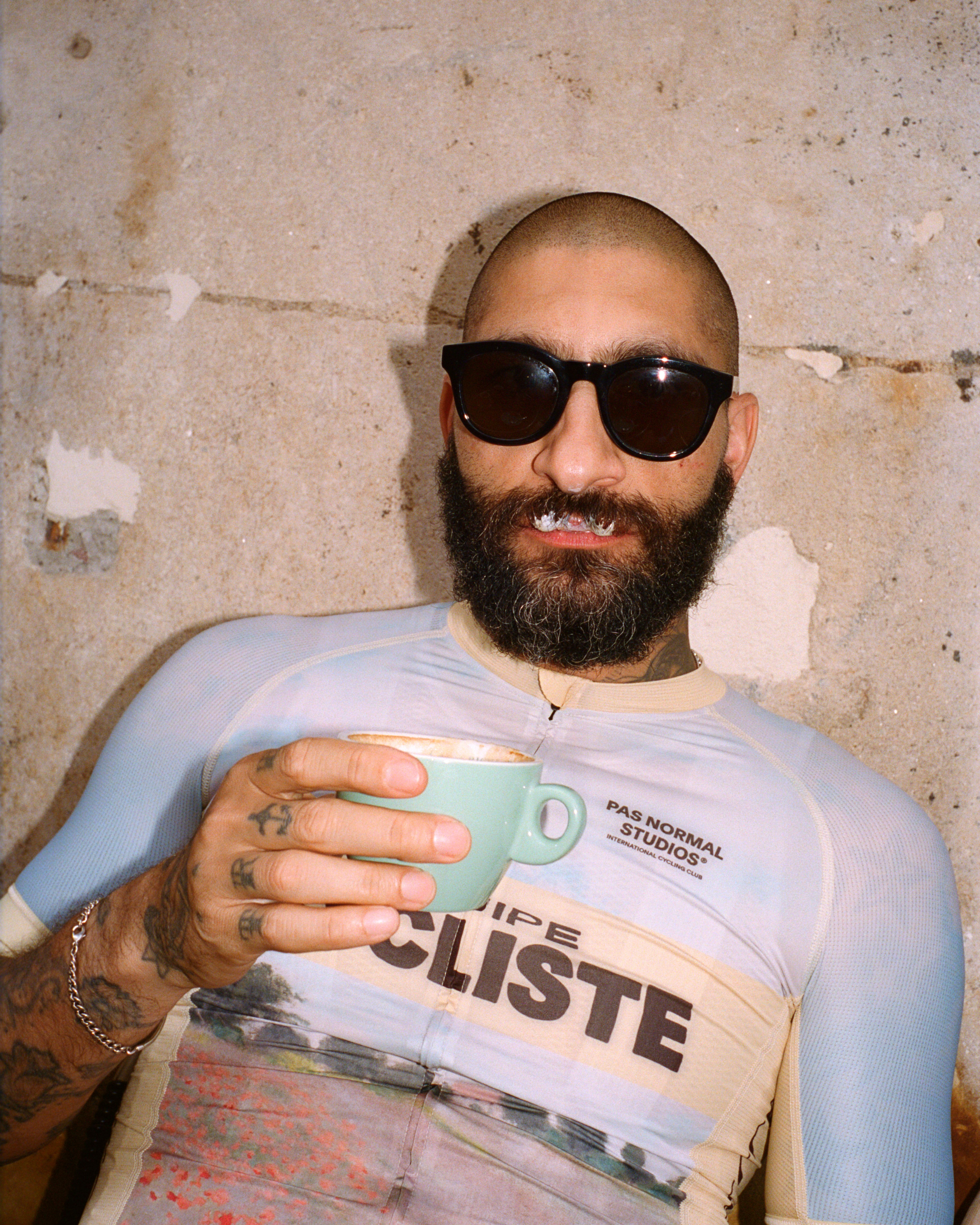 Model wearing white long sleeve top with graphic print and logo branding, holding mint green coffee cup
