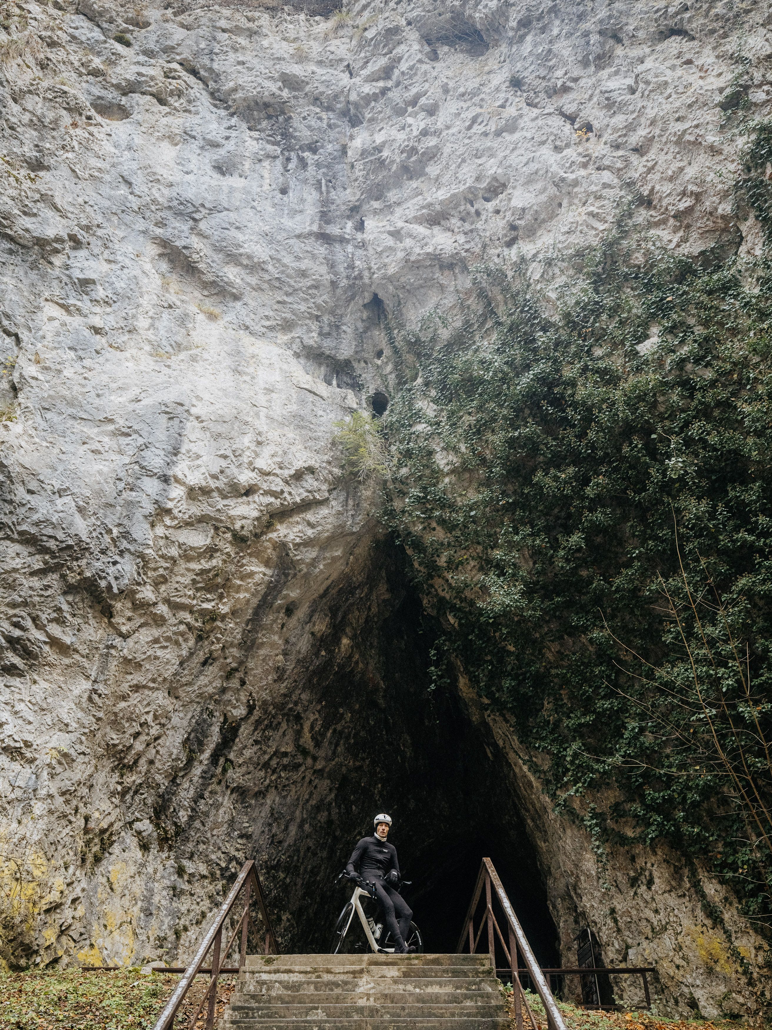 Cyclist in black apparel standing on wooden bridge at canyon entrance with limestone cliffs