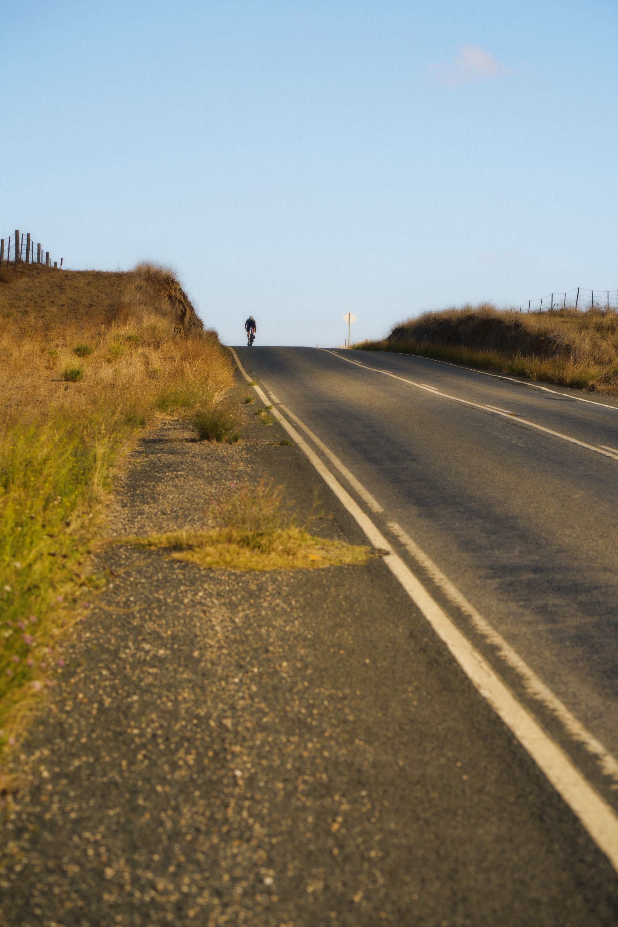 Cyclist on rural coastal road with golden grass hills