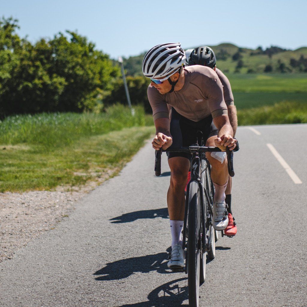 Model wearing brown cycling jersey and black shorts on time trial bike on rural road