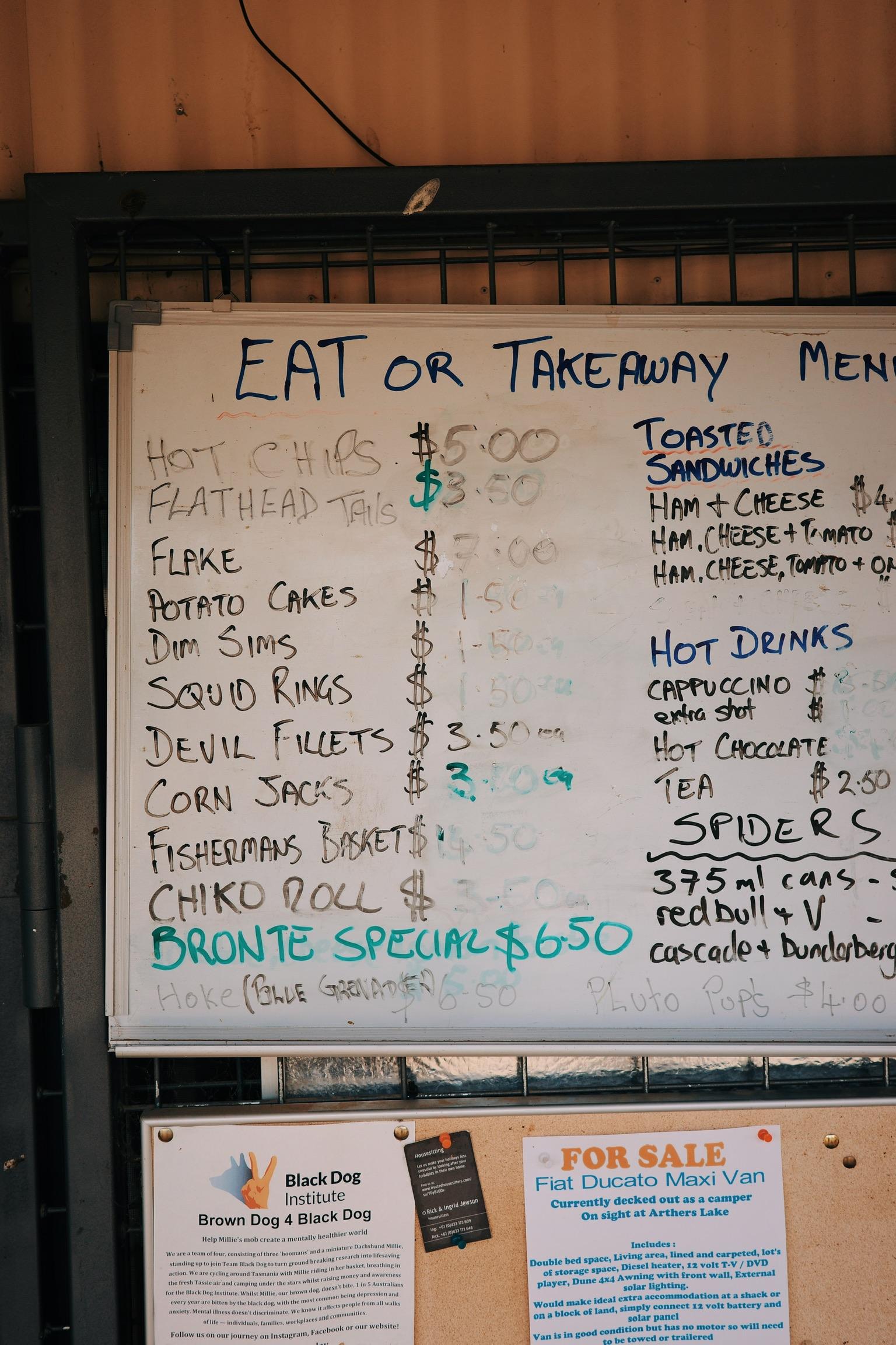 Restaurant menu board showing eat-in and takeaway options with fish and chips, sandwiches, and hot drinks