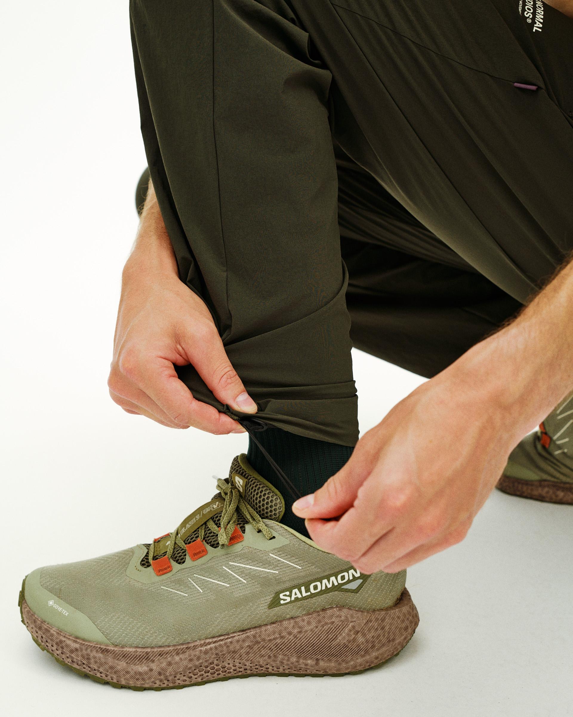 Green Balance pants on model adjusting cuff with textured sole running shoe