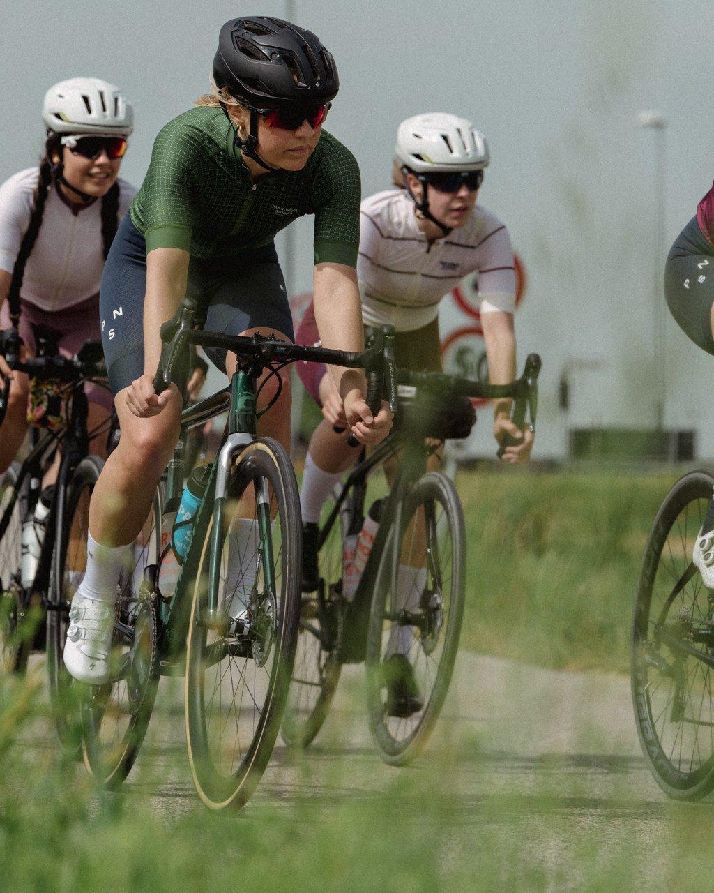 Model wearing green cycling jersey in aerodynamic position during group ride on wet road