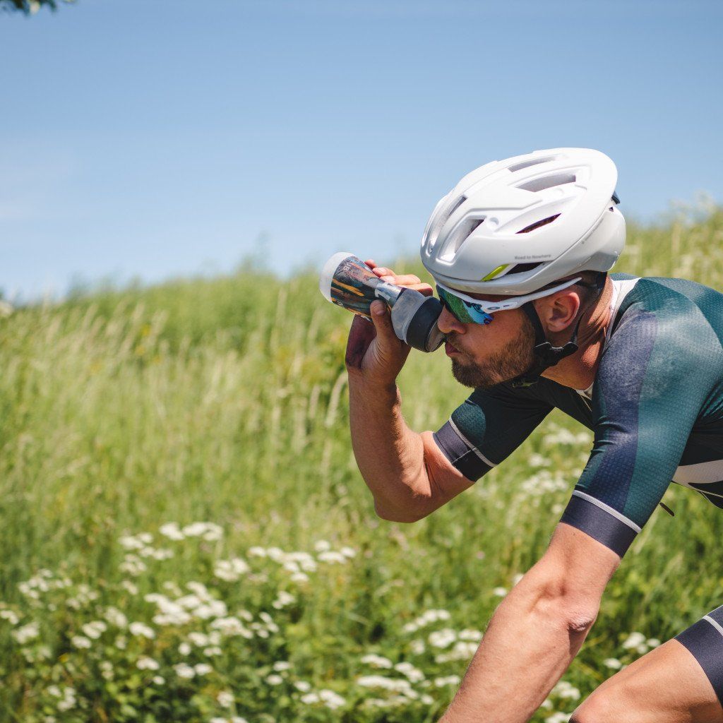 Model wearing teal and navy cycling jersey drinking from bottle in natural outdoor setting
