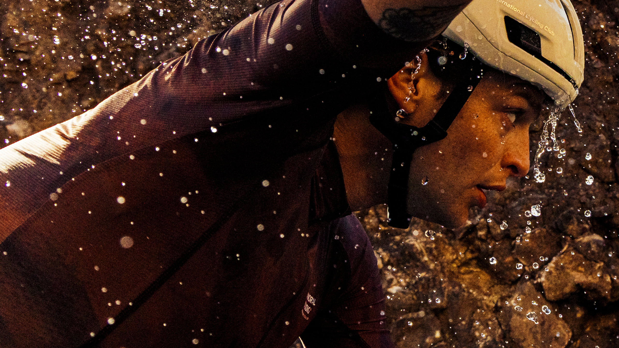 Model wearing dark cycling jersey and helmet in water with splashing droplets