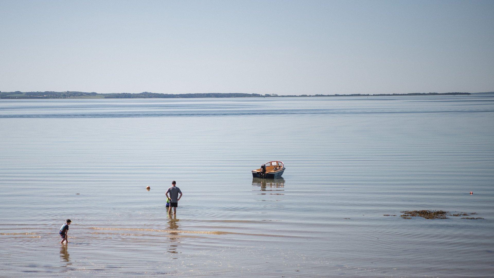 Calm coastal scene with people wading in shallow water near anchored boat