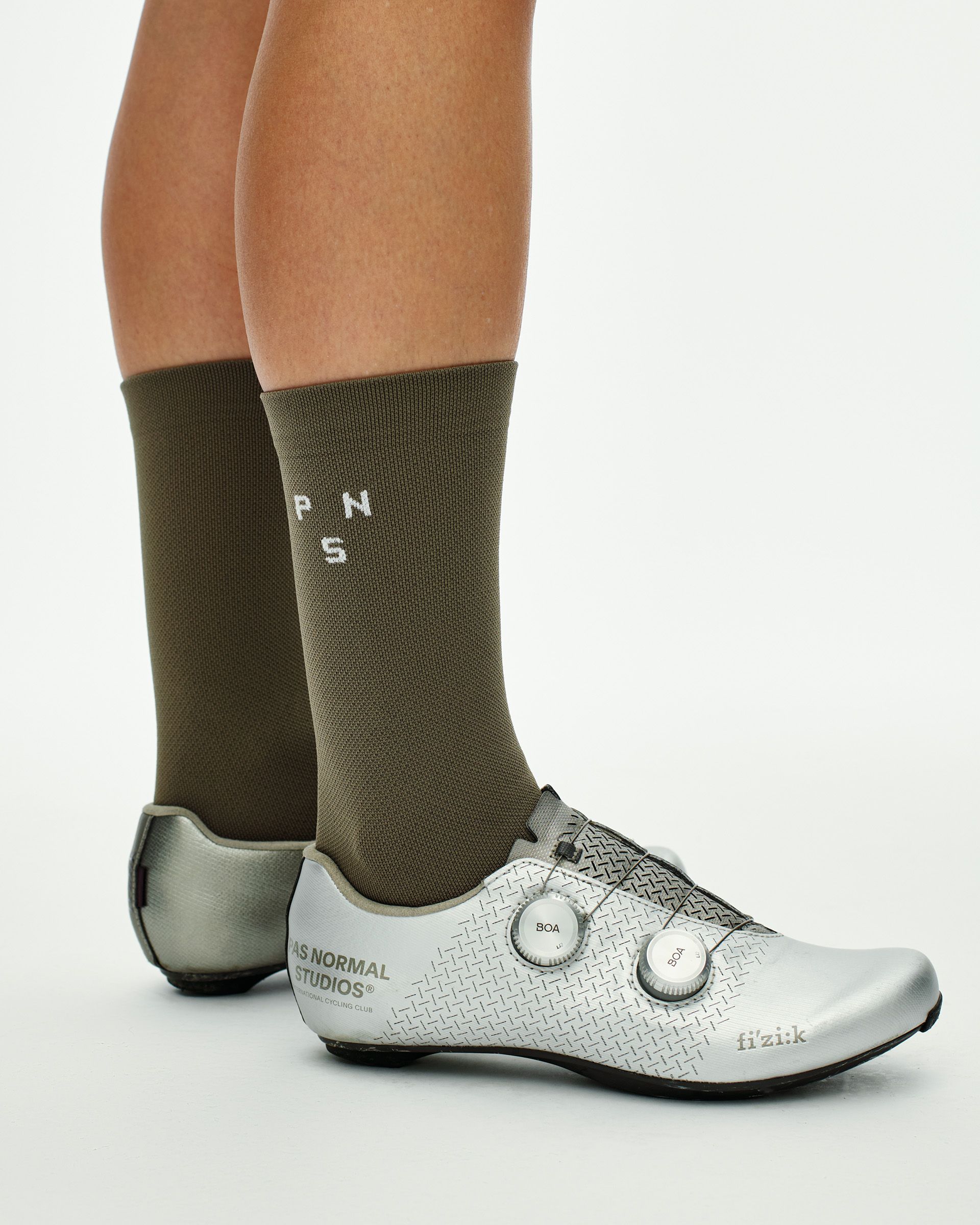 Earth khaki Essential cycling socks on model, side view with white PNS logo knit, worn with silver Fizik road shoes