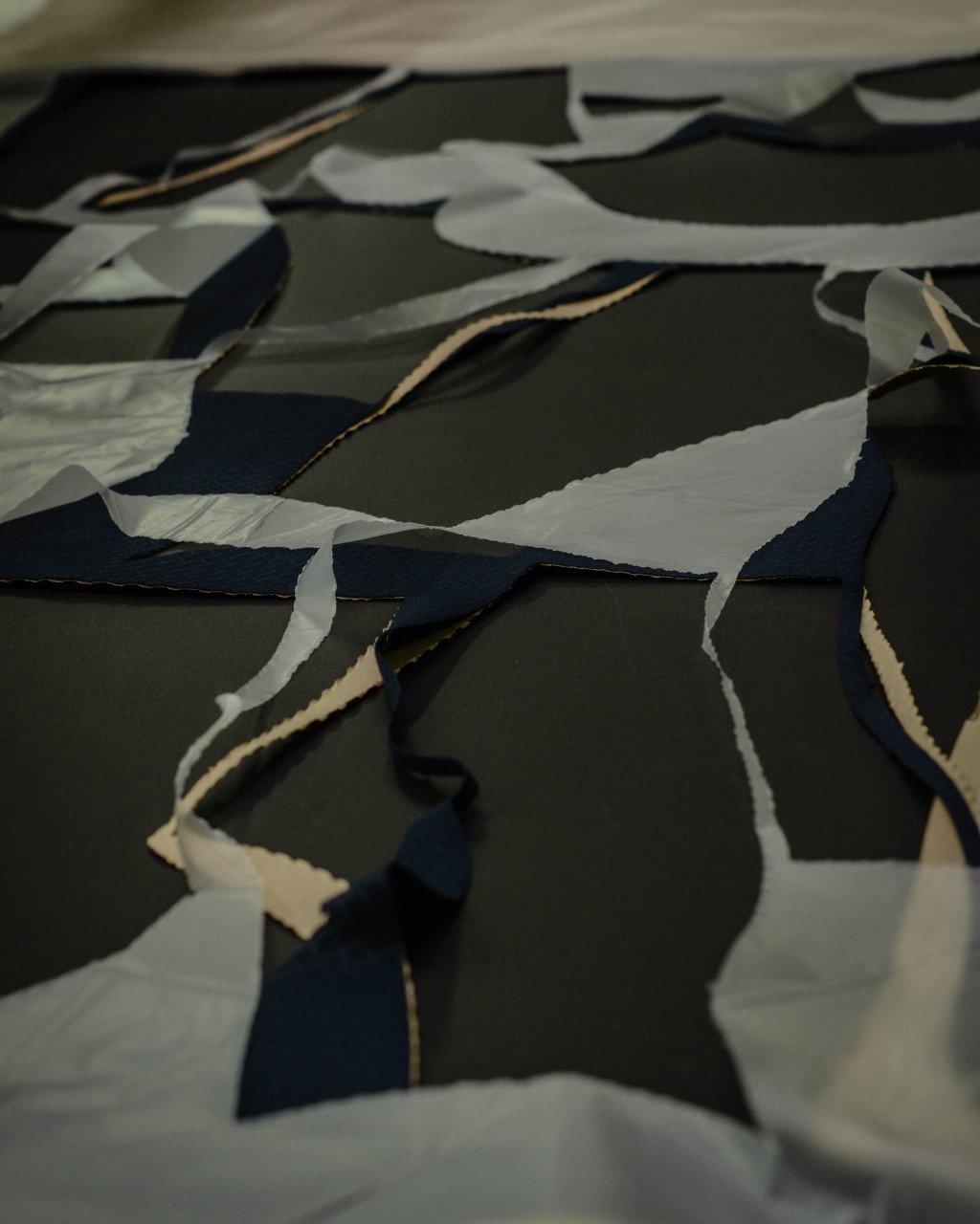 Layered fabric pieces in grey, navy, and cream tones arranged in an abstract pattern