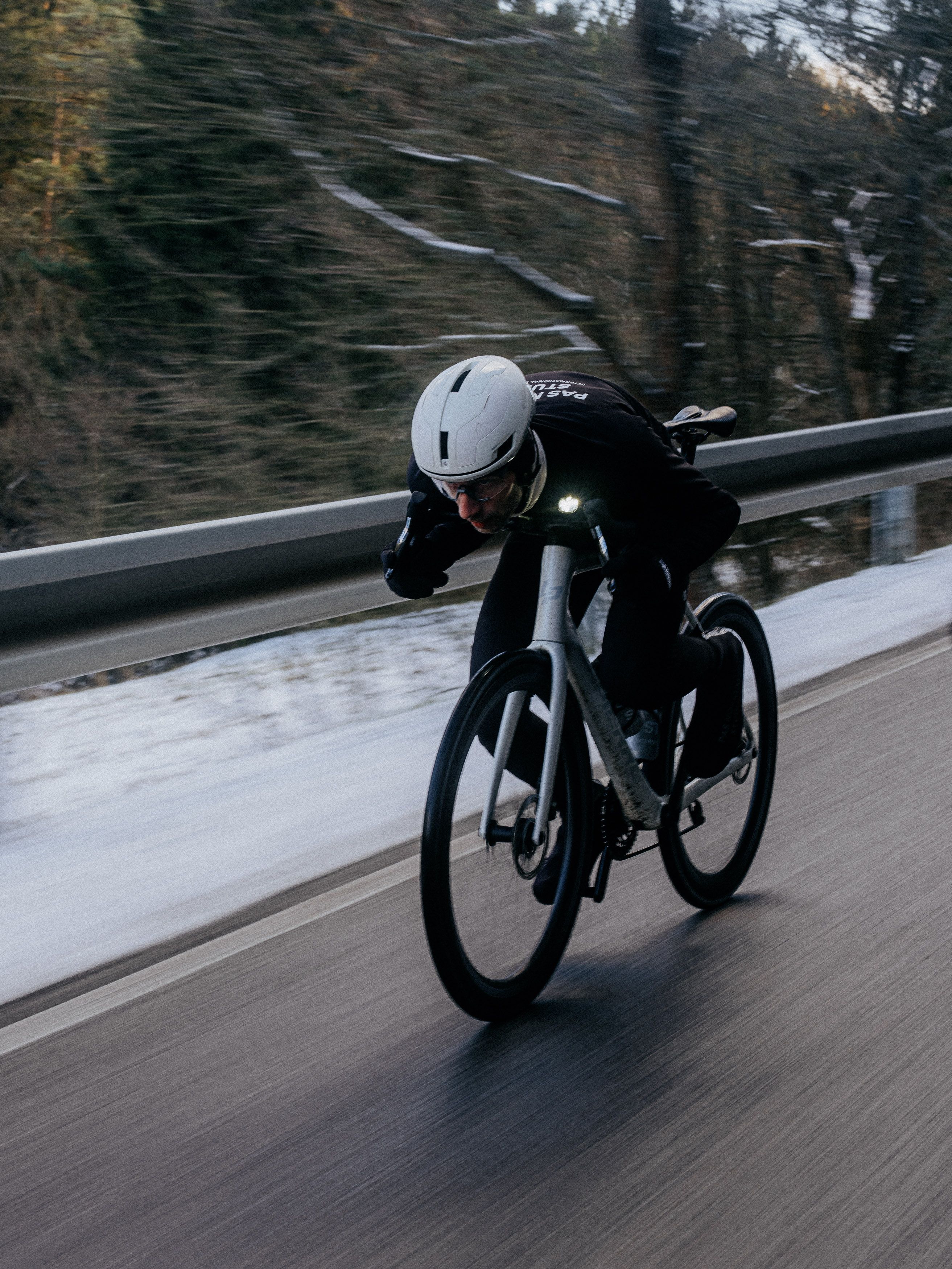 Cyclist in aerodynamic position on time trial bike wearing black kit and white helmet on road