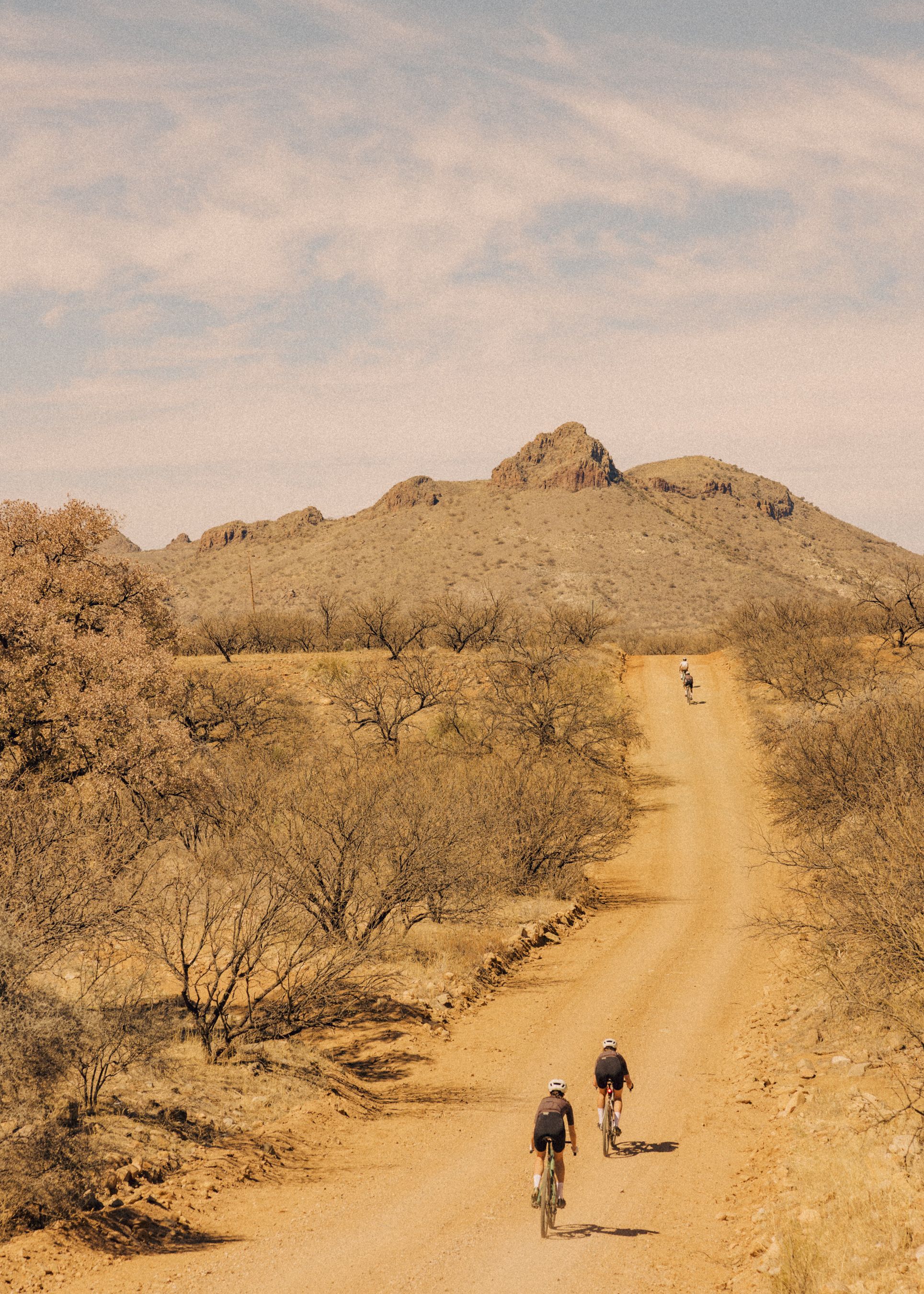 Cyclists riding on dirt road through desert landscape with mountains in background