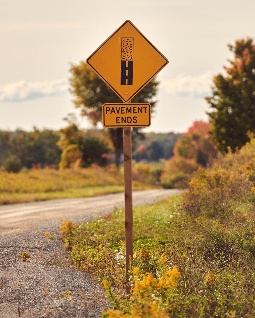Pavement ends road sign on autumn rural road with fall foliage