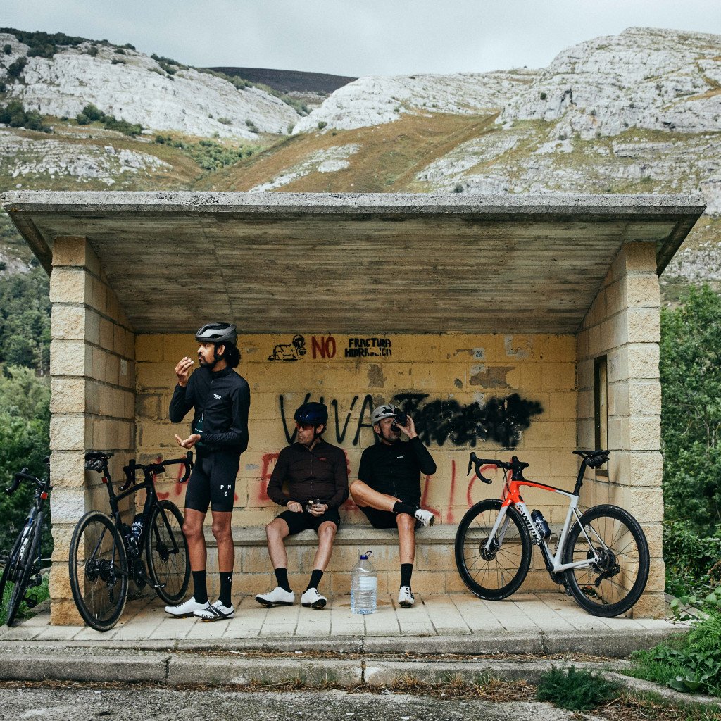 Three cyclists taking a rest break at roadside shelter with bikes in mountainous terrain