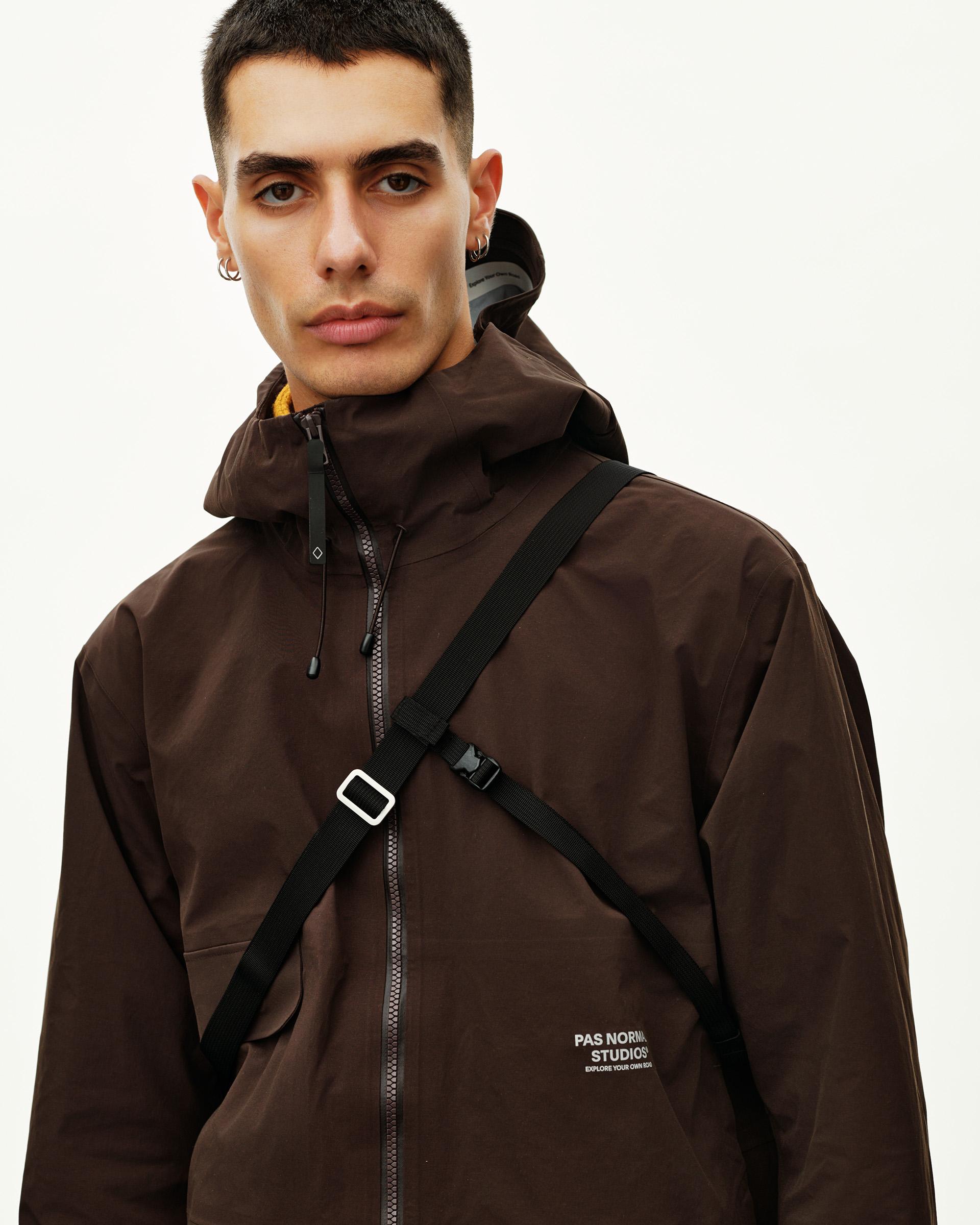 Black Off-Race Tech Musette 2.0 bag on model worn as cross-body harness over brown hooded jacket