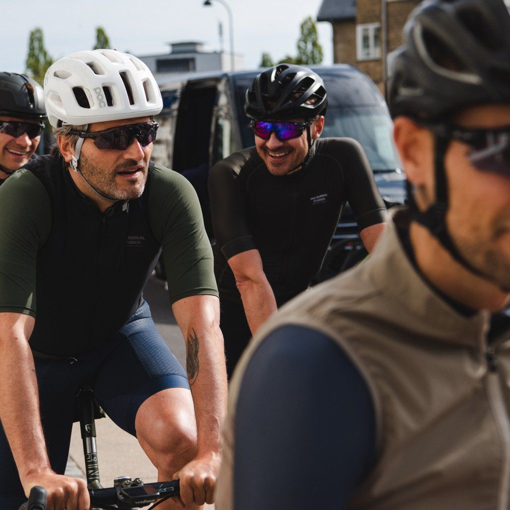 Model wearing green Mechanism Jersey and blue shorts with white helmet among group of cyclists