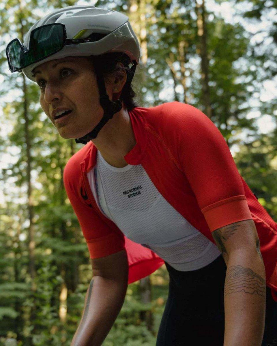 Model wearing red cycling jersey with white mesh panel and aero helmet in wooded setting