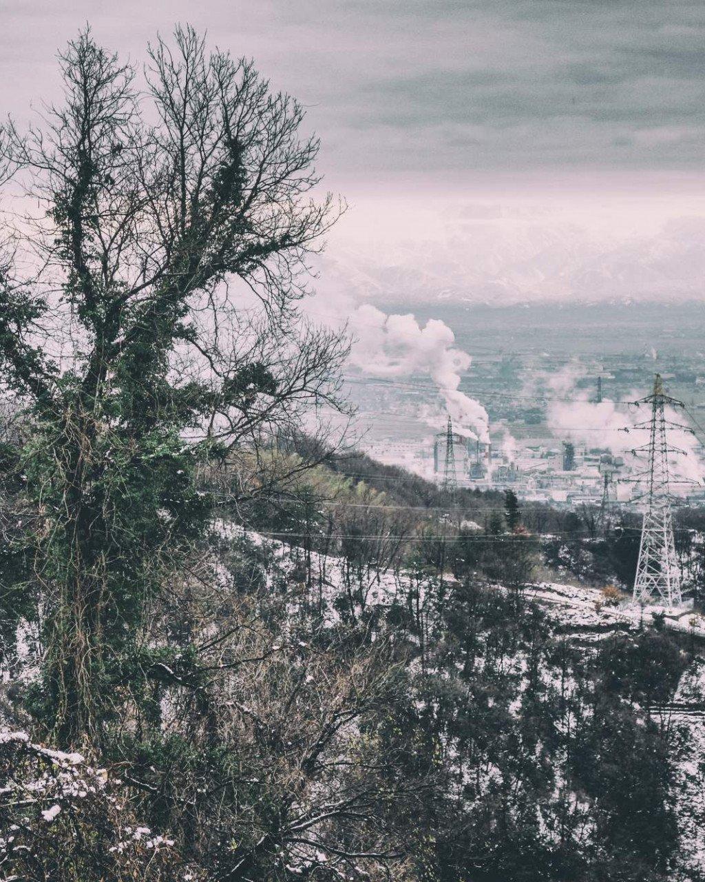 Winter landscape view of Toyama, Japan with bare trees, snow-covered hills and industrial buildings in distance