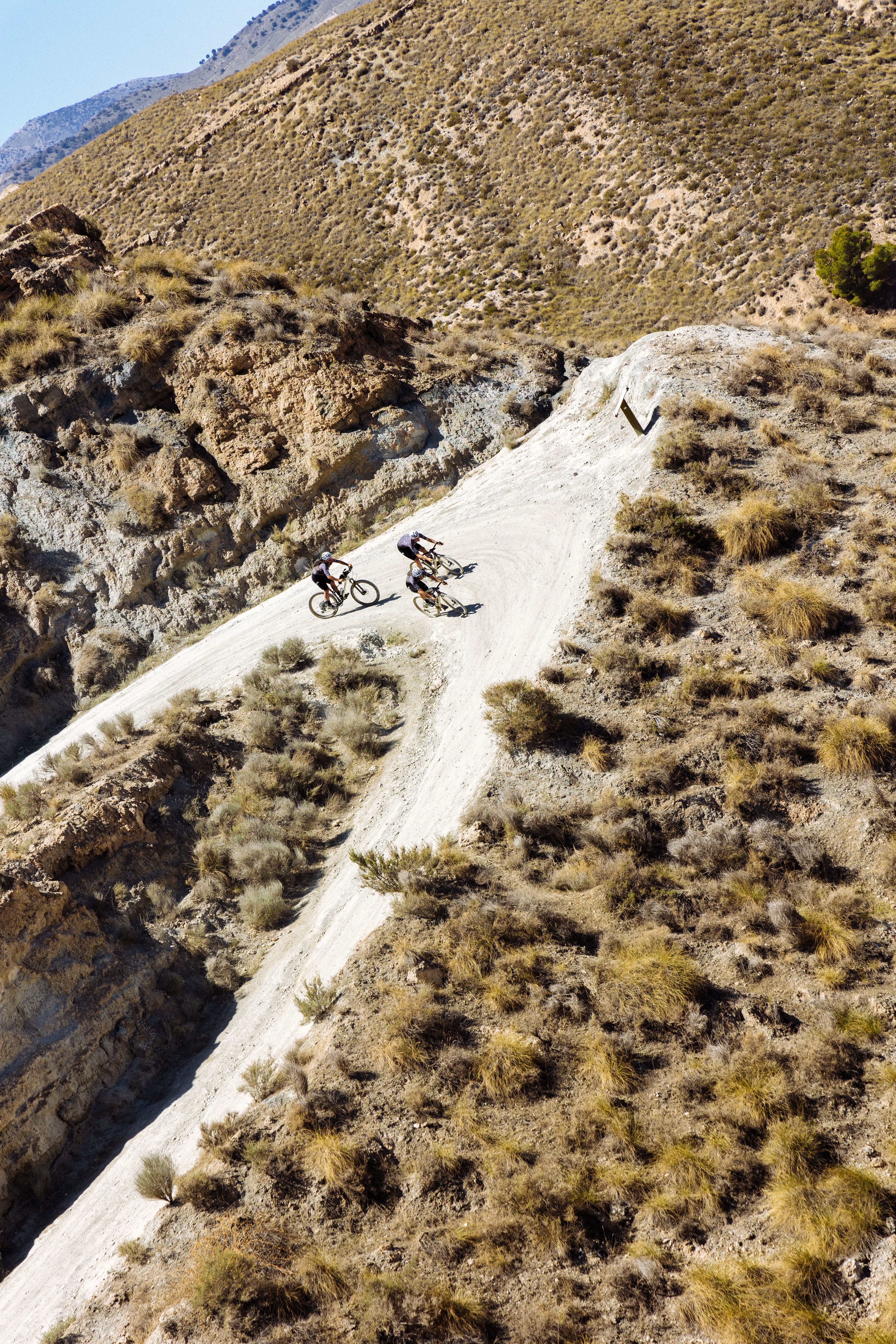 Two cyclists riding on mountain road through arid landscape with rocky terrain and sparse vegetation