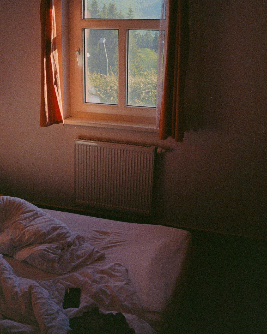 Sunlit bedroom interior with unmade bed and window overlooking green landscape