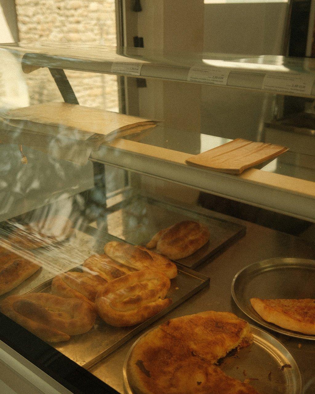 Bakery display case with fresh pastries and bread on wooden shelves behind glass