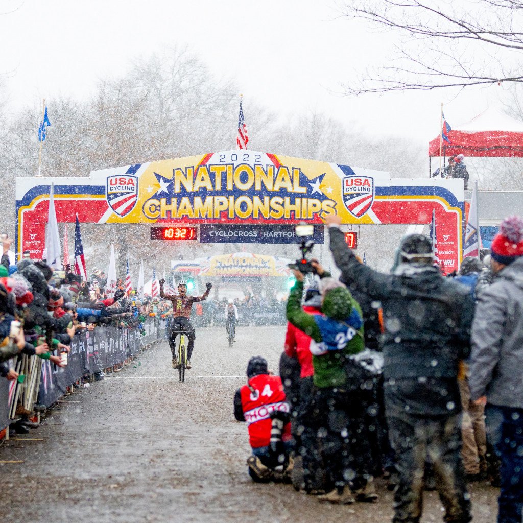 Cyclocross racer crossing finish line at 2022 National Championships in snowy conditions with spectators