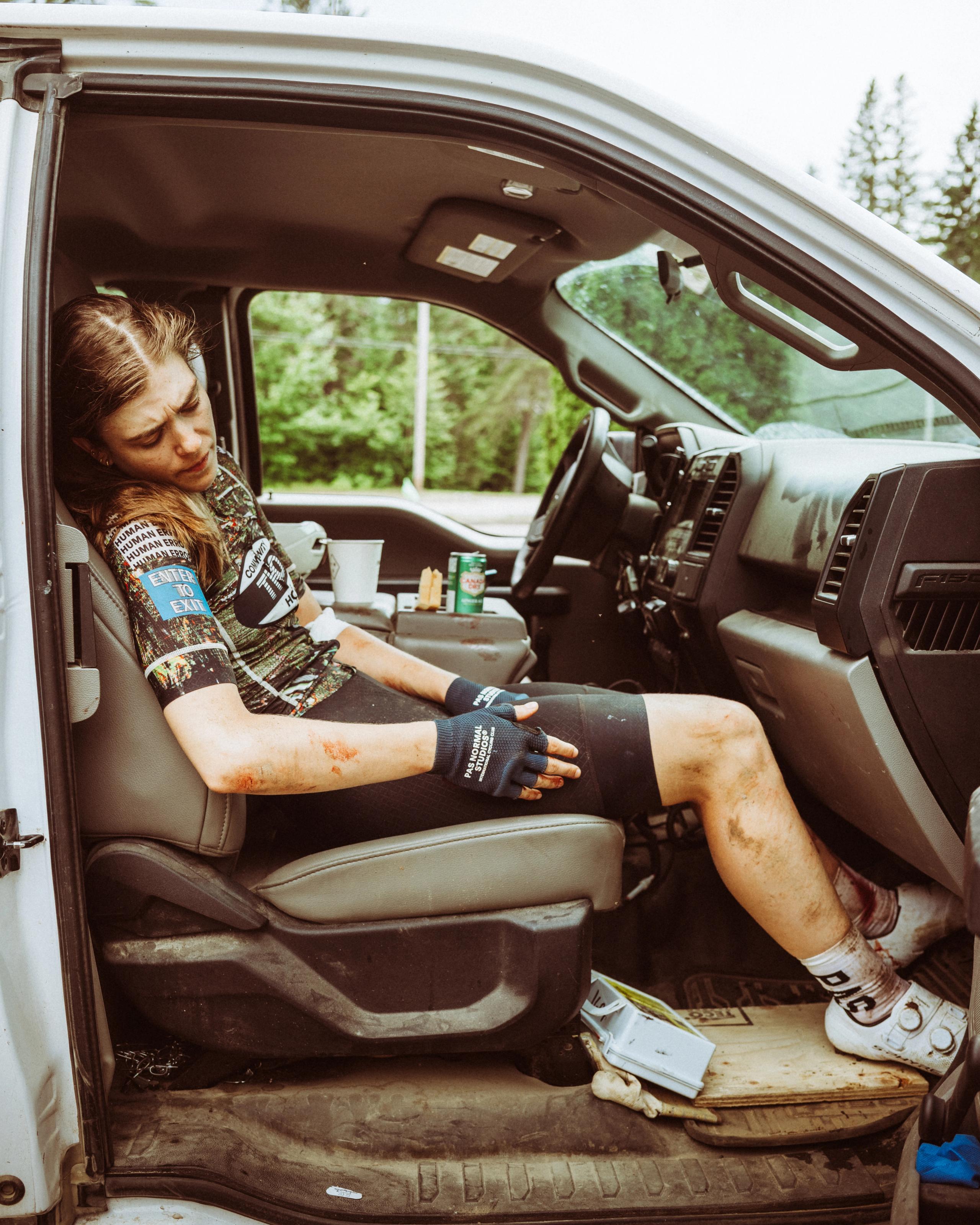 Model wearing patterned jersey and black cycling shorts with fingerless gloves, resting in van interior after ride