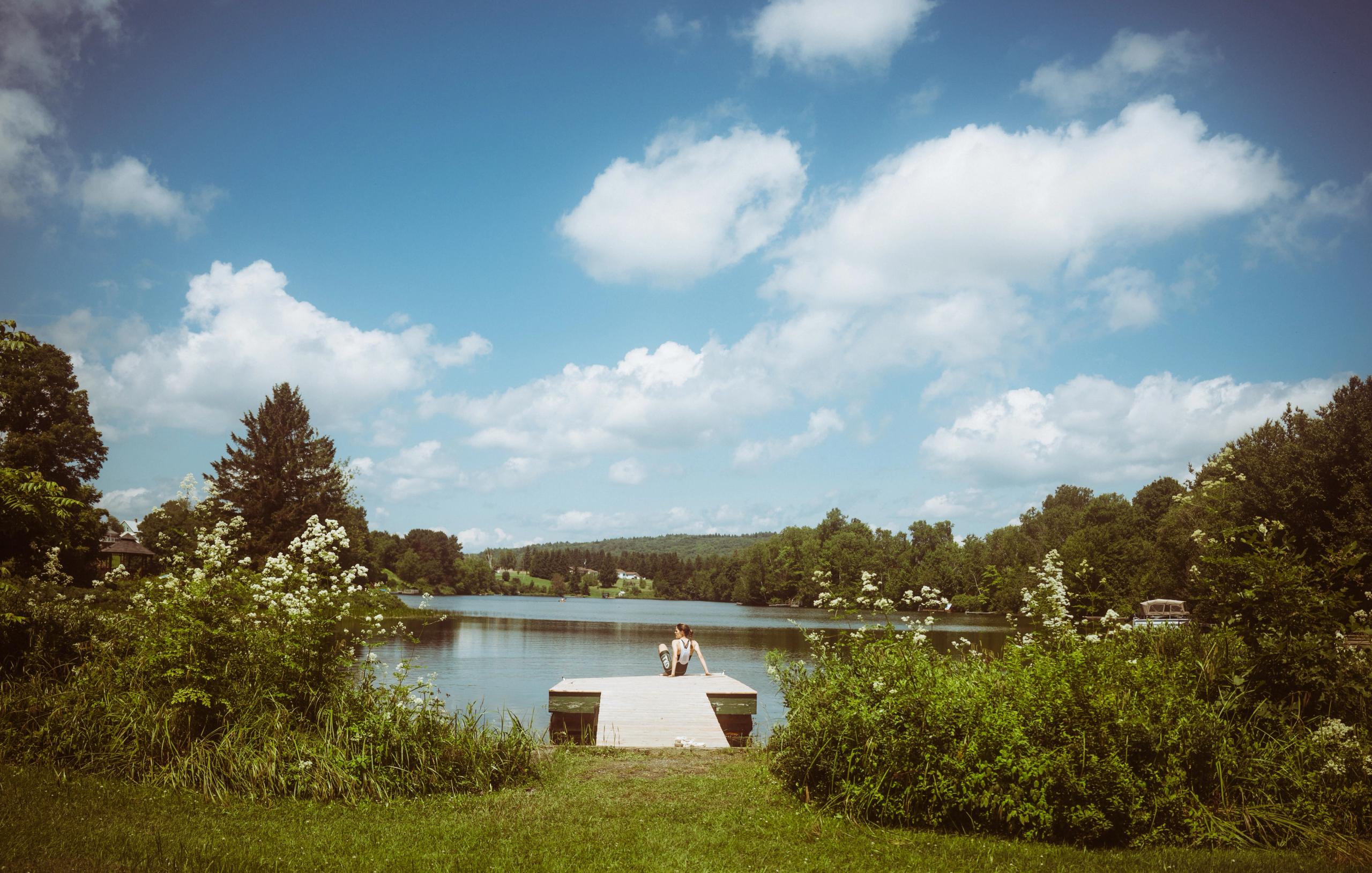 Cyclist resting on lakeside dock surrounded by lush greenery under blue sky with white clouds