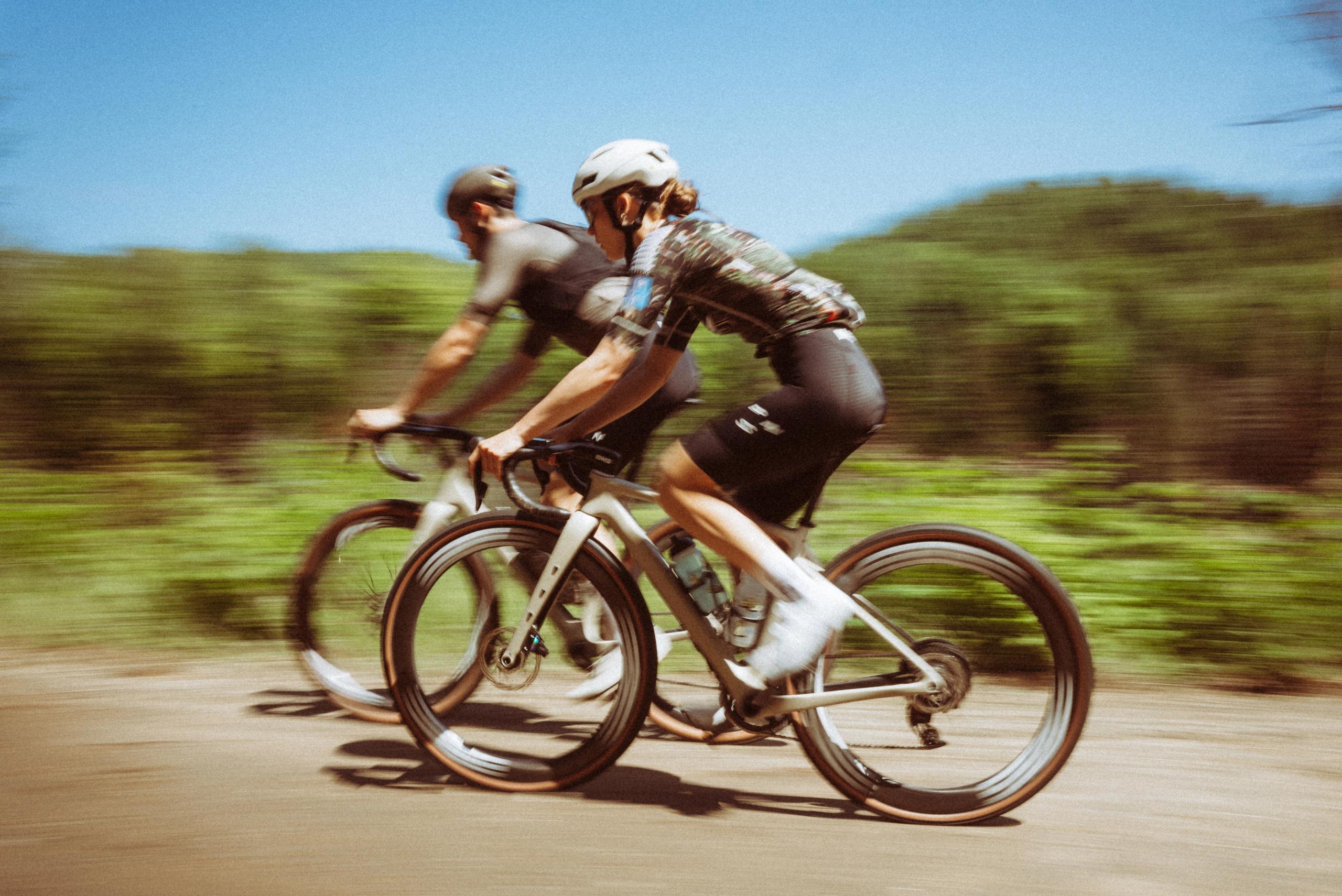 Two cyclists in dark cycling kit riding on rural road with motion blur