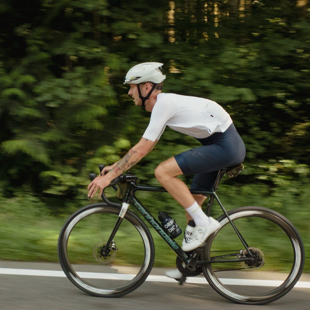 Model wearing white cycling jersey and dark blue shorts on road bike in aerodynamic position
