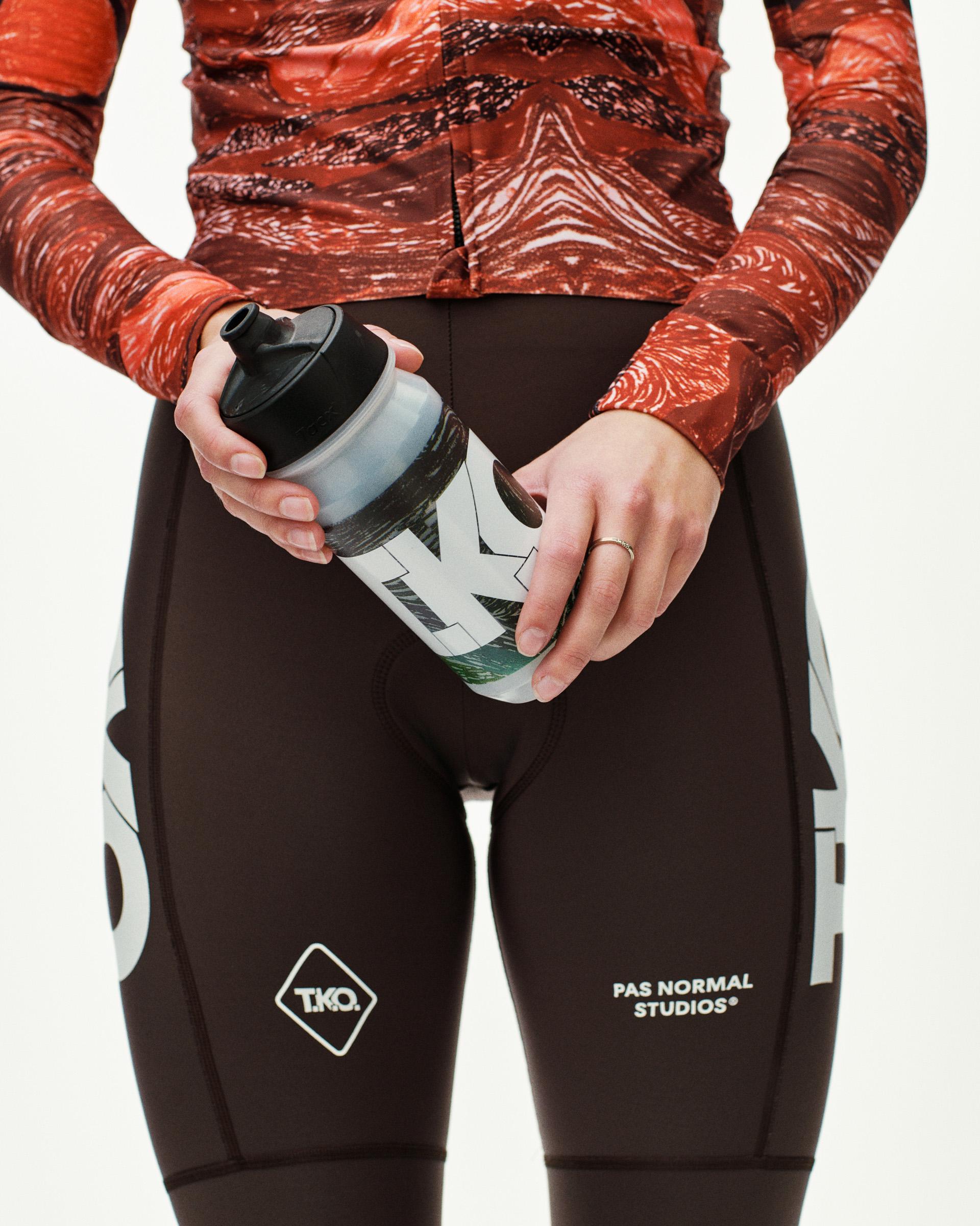 Dark Multi T.K.O. cycling water bottle held by model, front view with graphic print and black cap