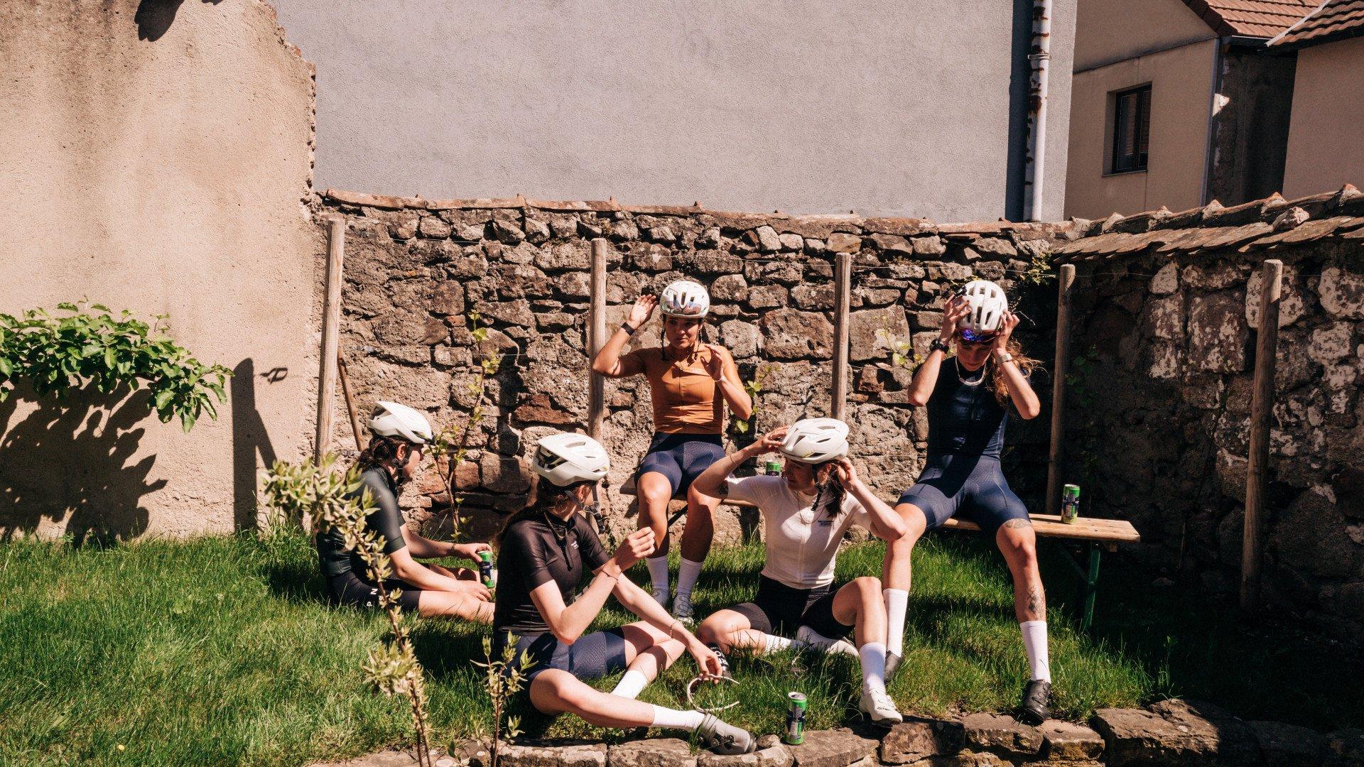 Group of female cyclists in cycling apparel resting on stone wall in Mediterranean village courtyard
