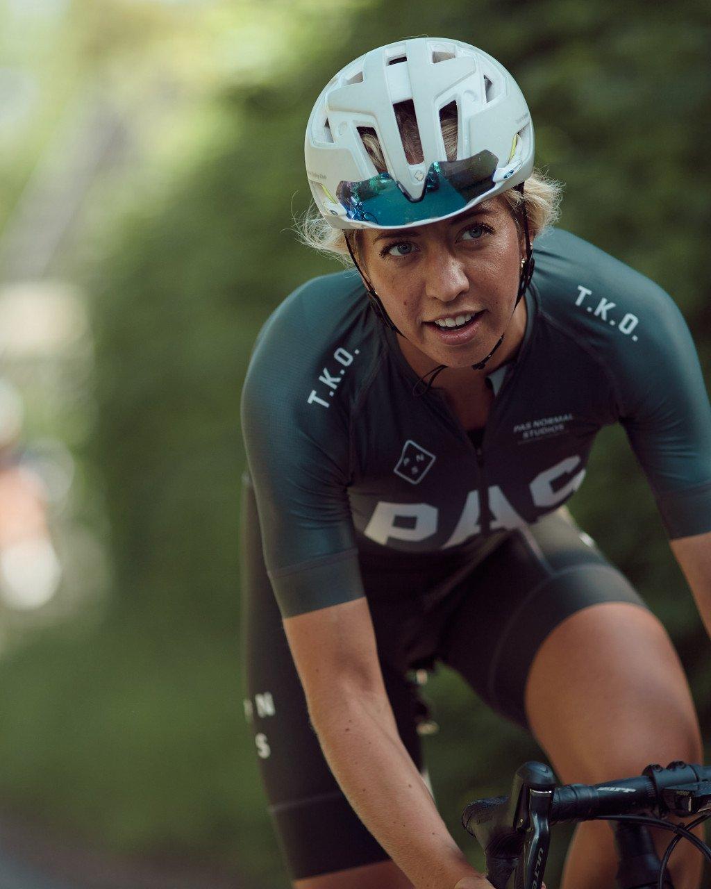 Model wearing Women's PAS Collection dark green jersey with white lettering in racing position with helmet