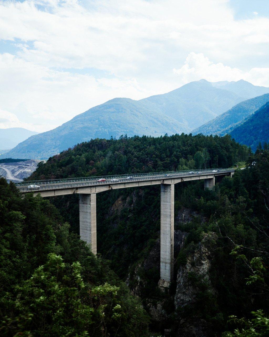 Highway bridge spanning forested valley with mountains in background