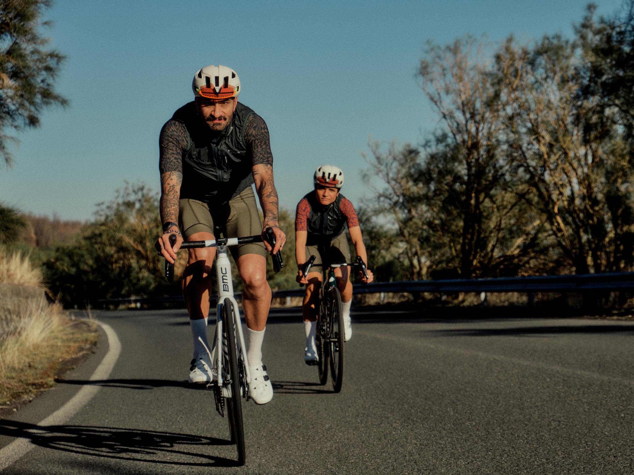 Two cyclists in aerodynamic position on time trial bikes wearing dark cycling kits and aero helmets on road