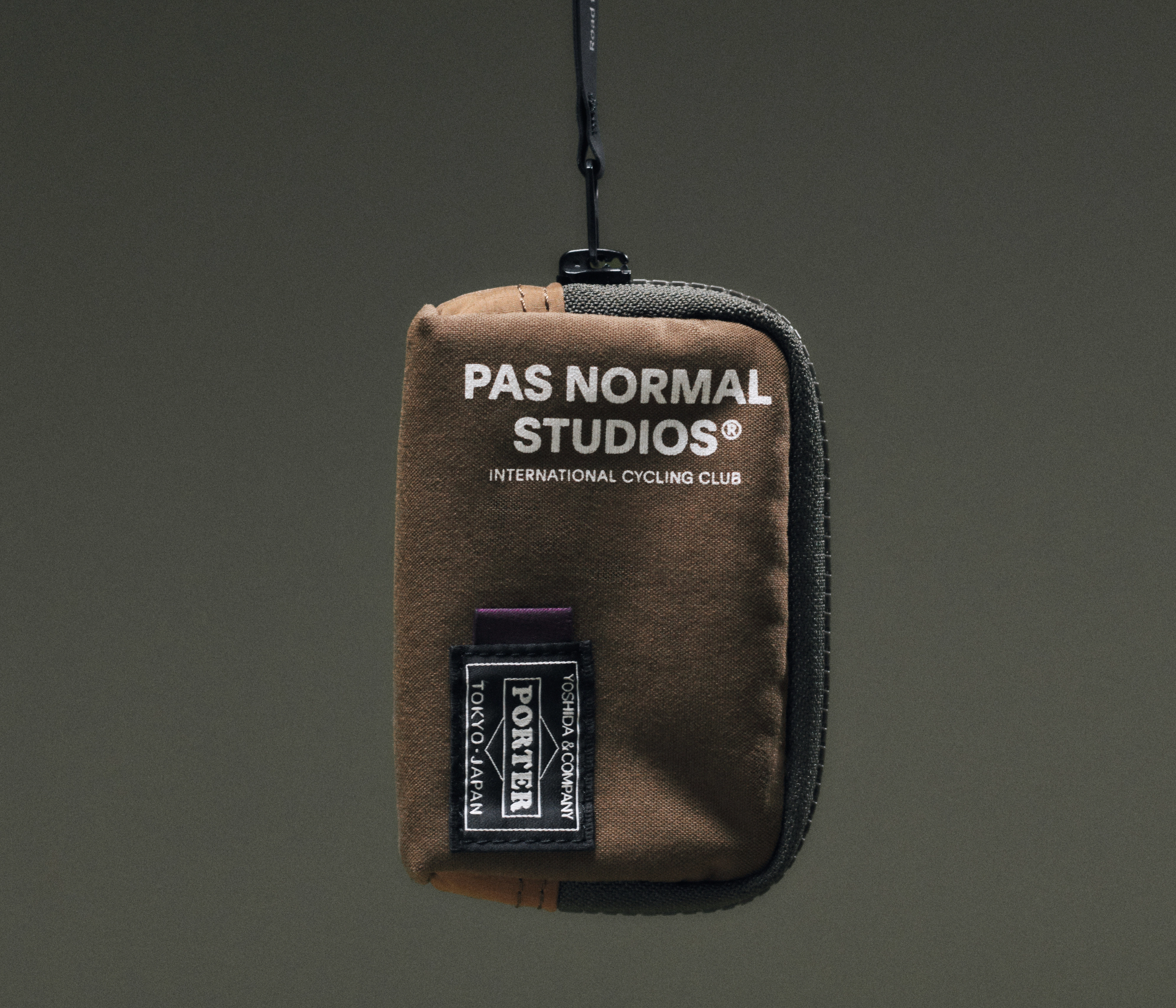Tan Porter-Yoshida coin case held up, front view with branded woven label and black clip hook