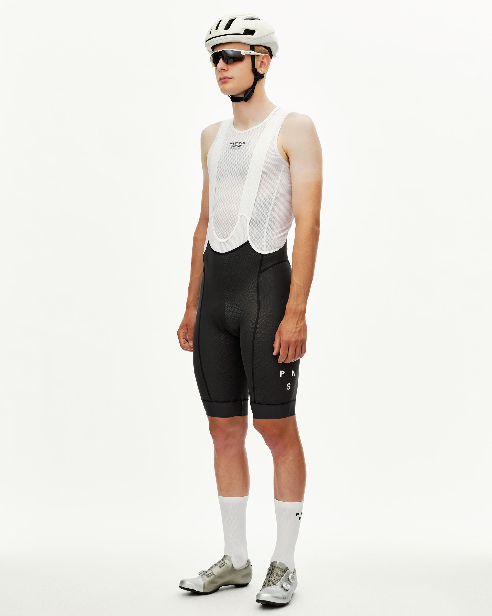 Dark Navy Mechanism cycling bibs on male model, three-quarter front view with white bib straps and logo leg print