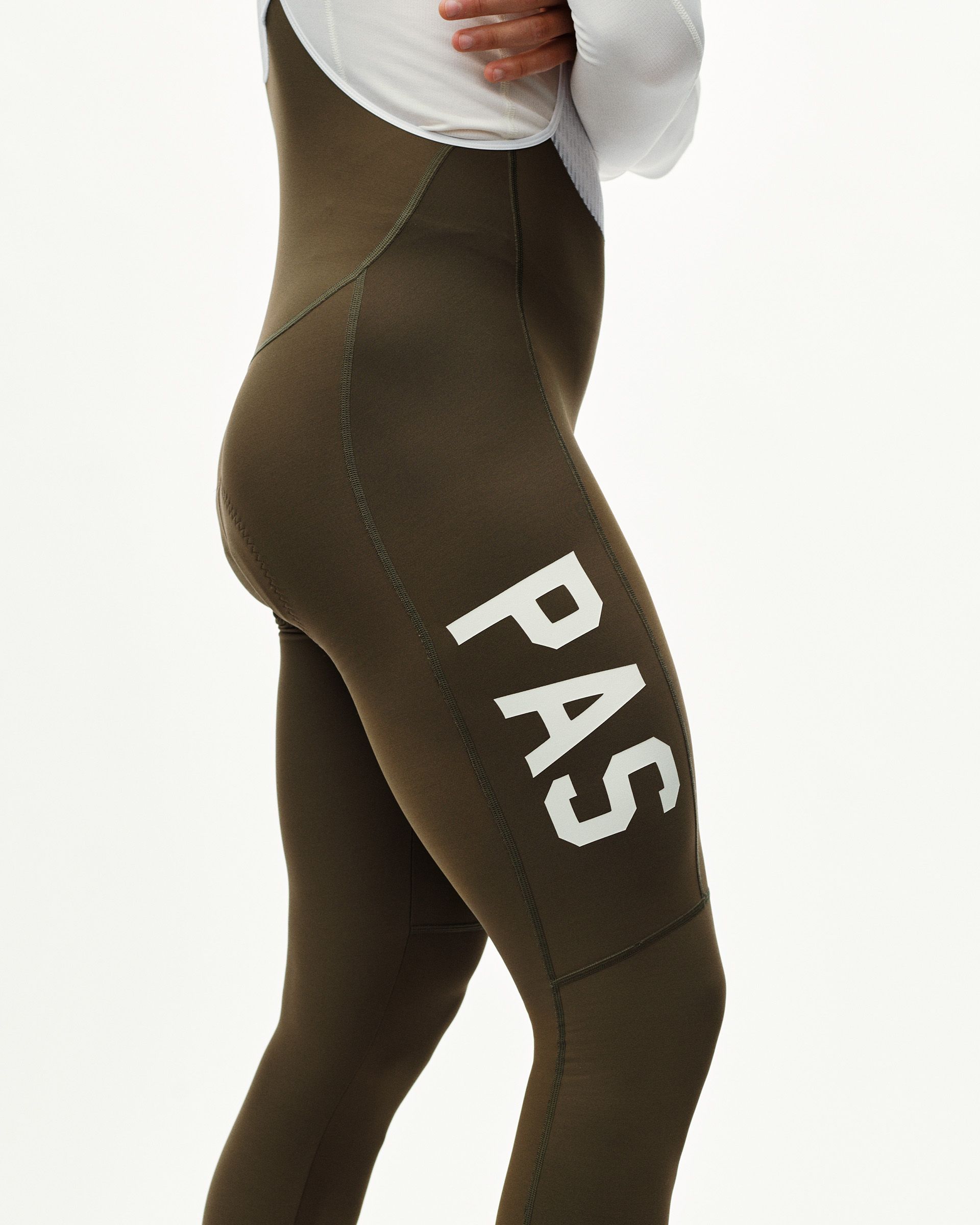 Dark Earth khaki PAS Mechanism Thermal Long cycling bibs on model, three-quarter rear view with white leg print