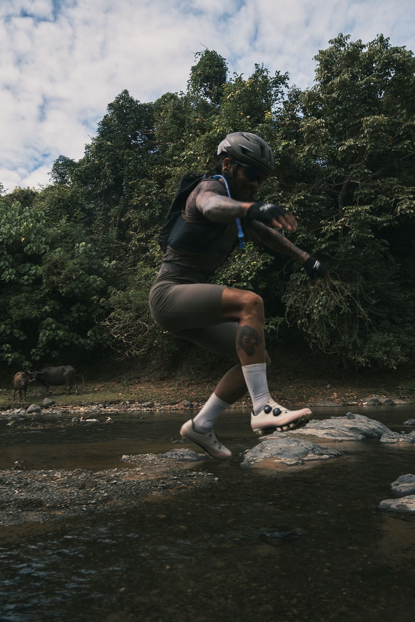 Cyclist running through creek wearing dark jersey and shorts with white socks