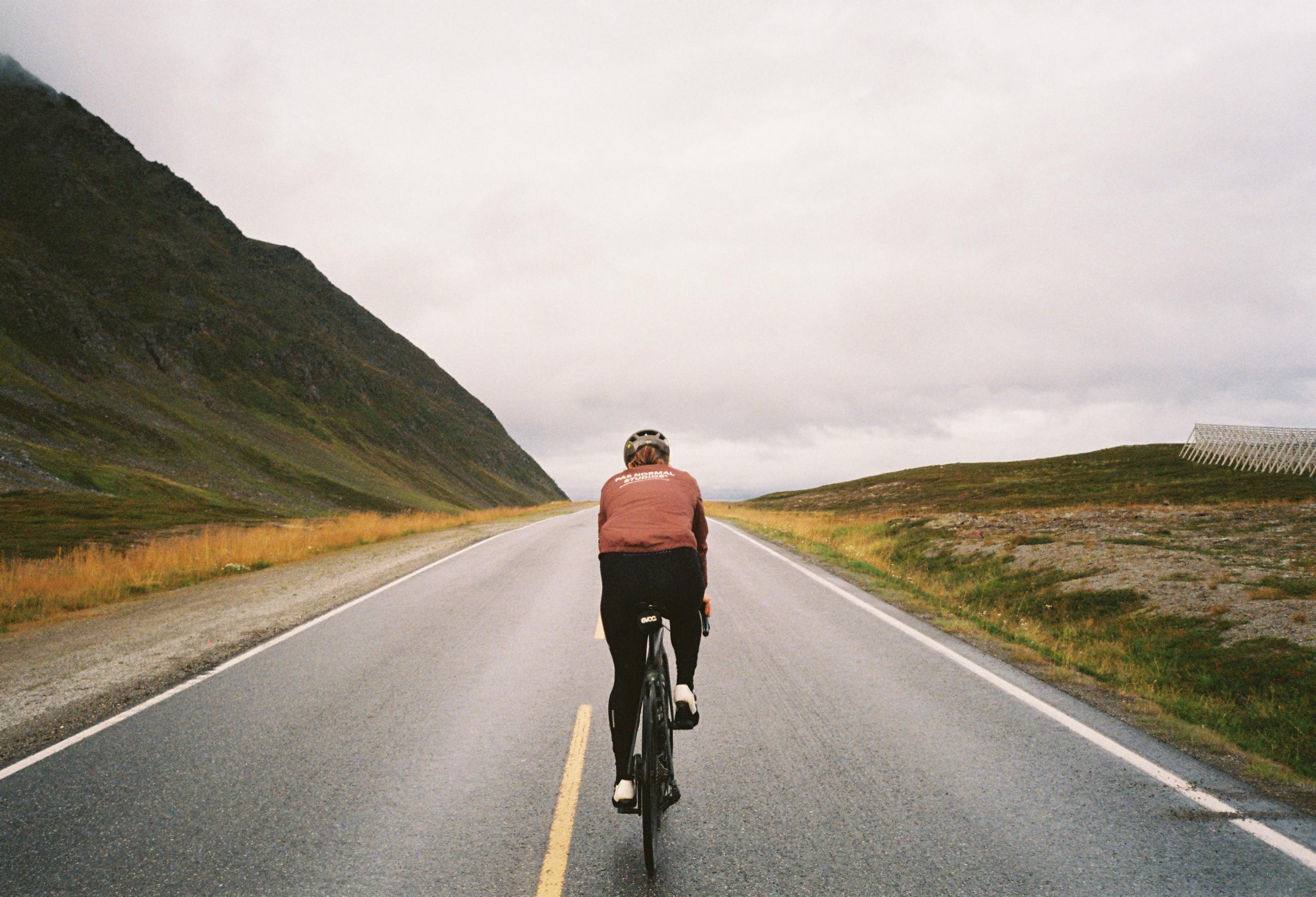Cyclist in rust-colored jersey and black tights riding on empty mountain road in Iceland