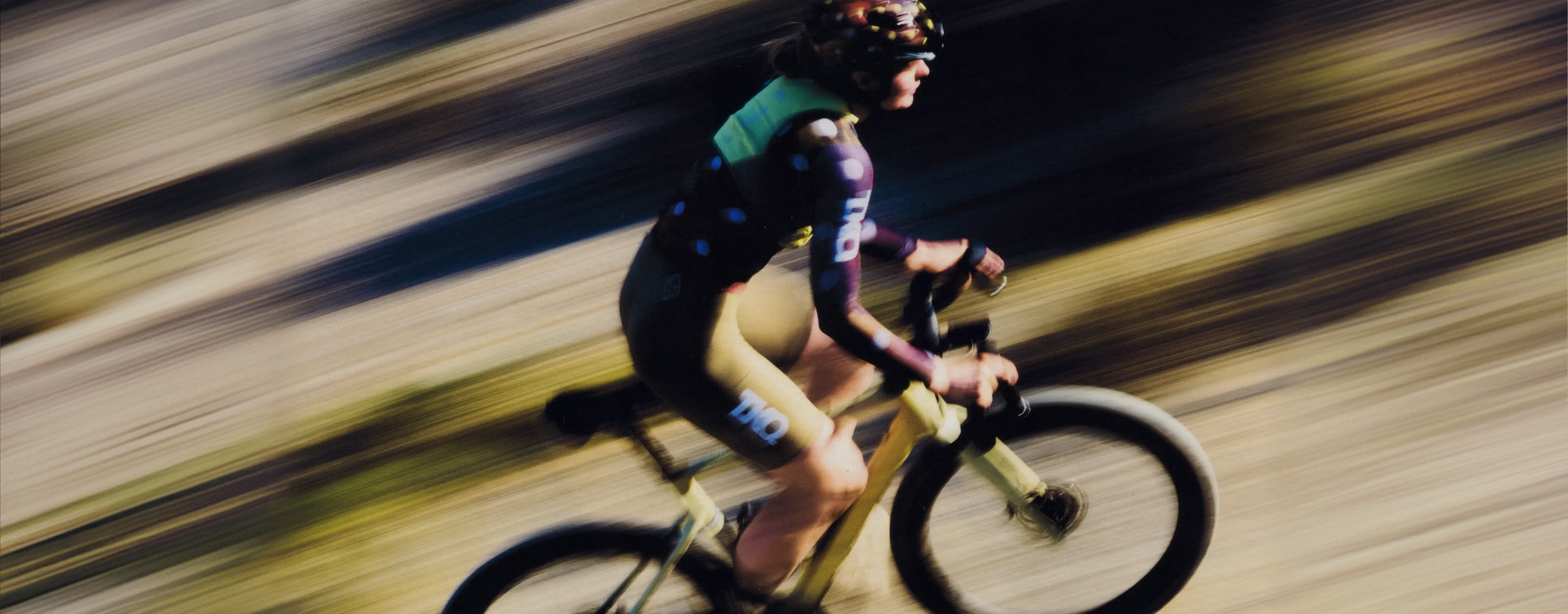 Model wearing T.K.O. collection with green jersey and black shorts cycling with motion blur