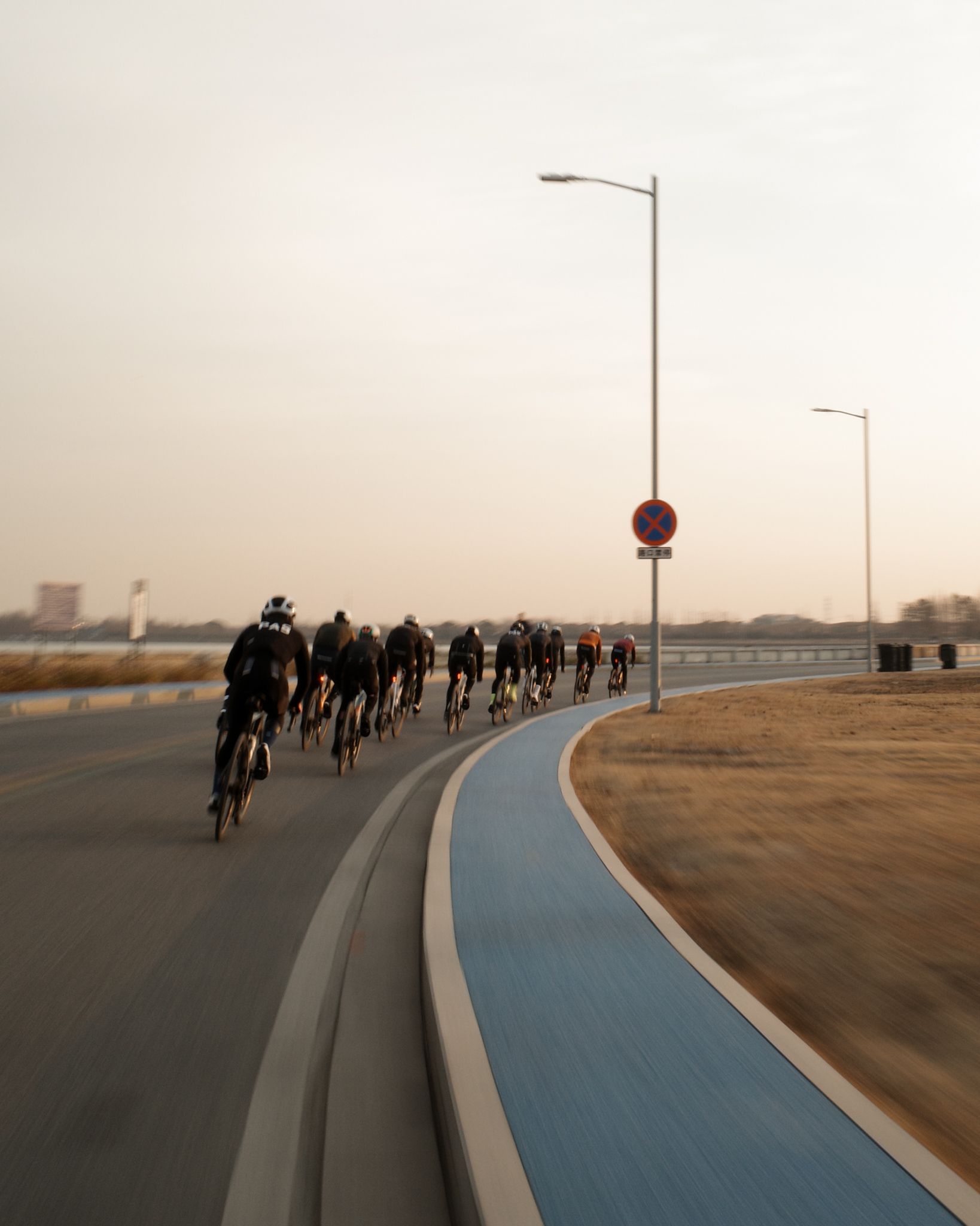 Group of cyclists in dark kit riding in formation on curved road with blue cycling lane