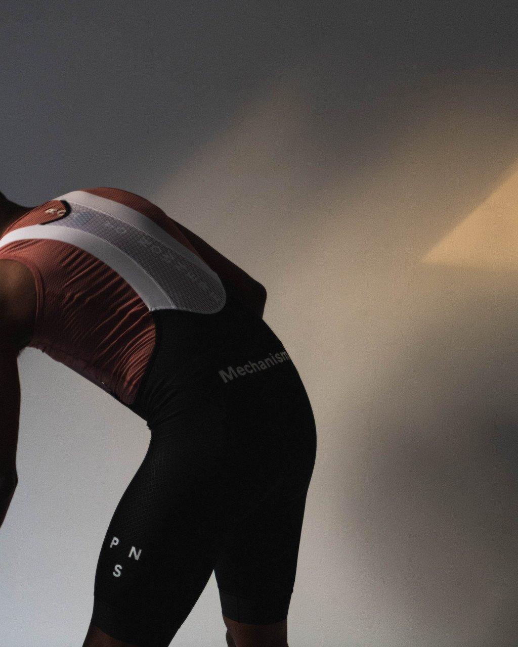 Model wearing Mechanism collection black cycling shorts with red and white jersey against dramatic sky