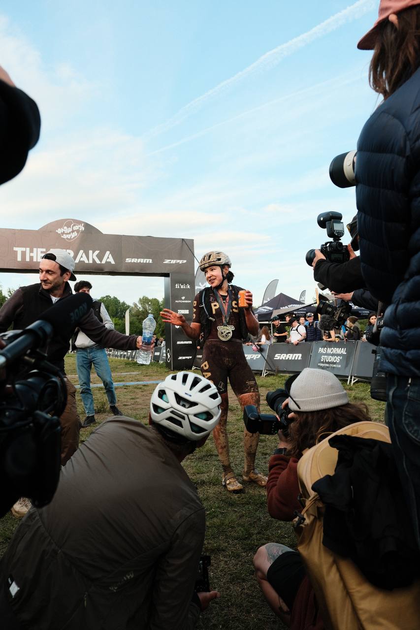 Cyclist being interviewed by media at Traka gravel race finish with sponsors banners in background