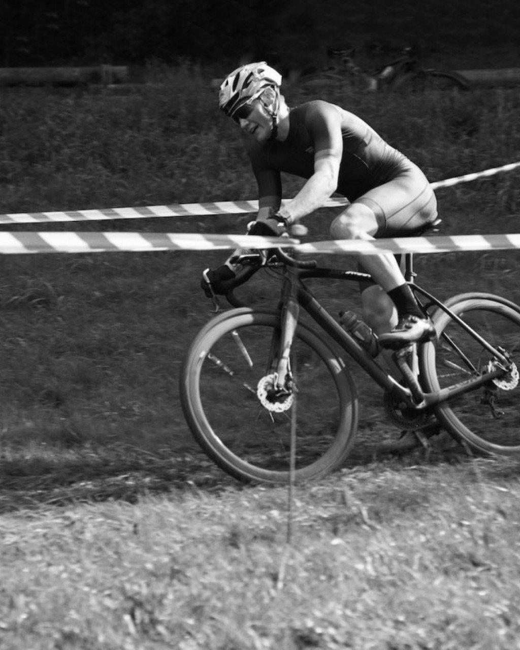 Model racing cyclocross in black skinsuit and helmet, navigating course barriers in black and white