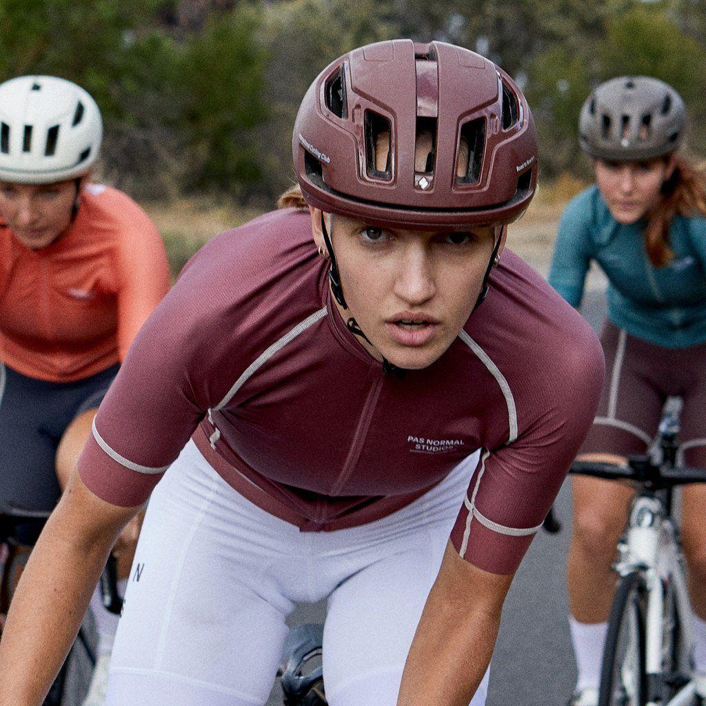 Model wearing maroon cycling helmet in aerodynamic position with cyclists in background