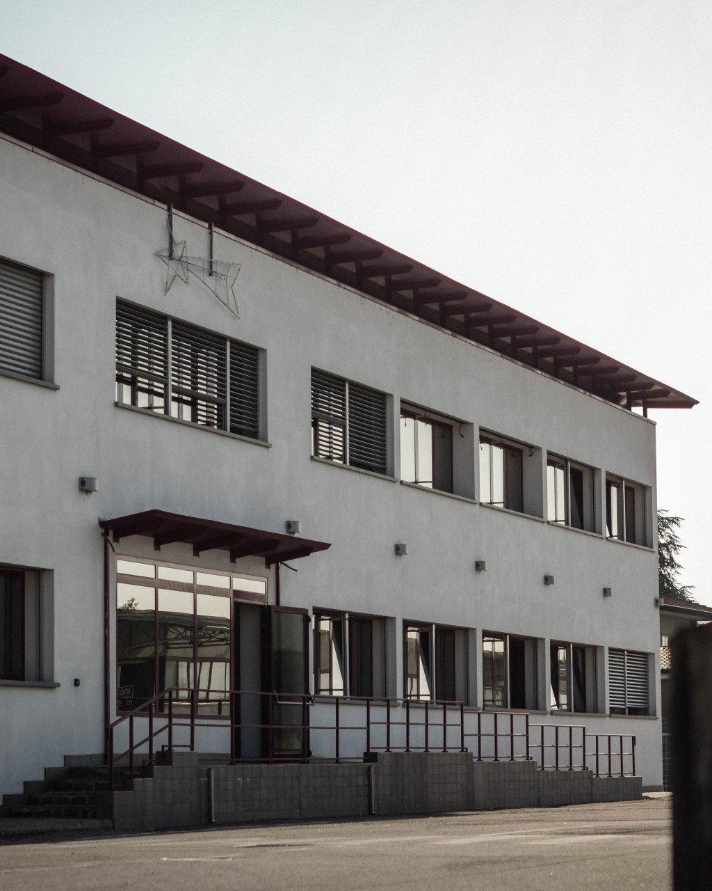Modern white building with dark roof and shutters, glass entrance with overhang and metal railings