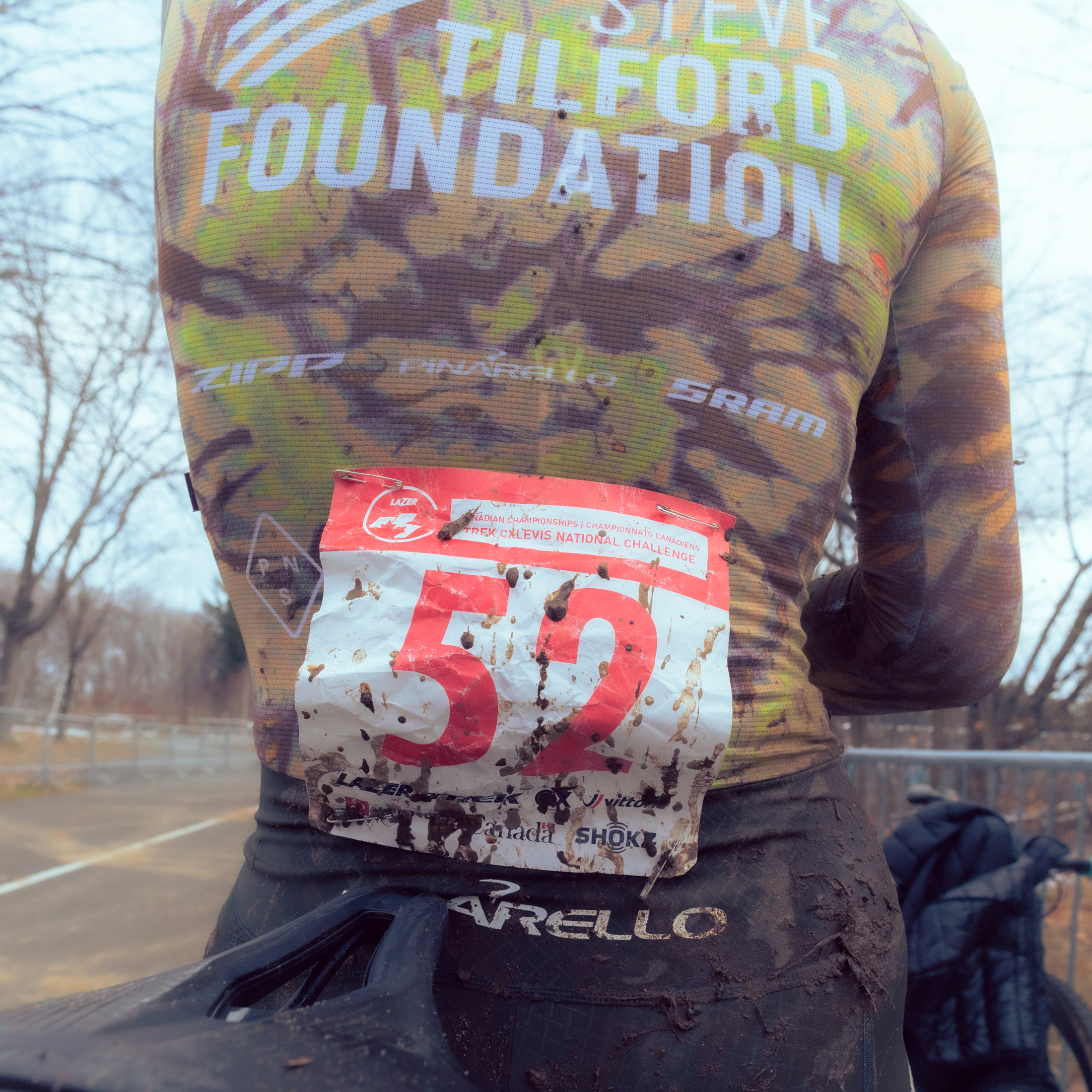 Model wearing mud-covered camouflage long sleeve jersey with race number 52, muddy cycling gear from cyclocross race